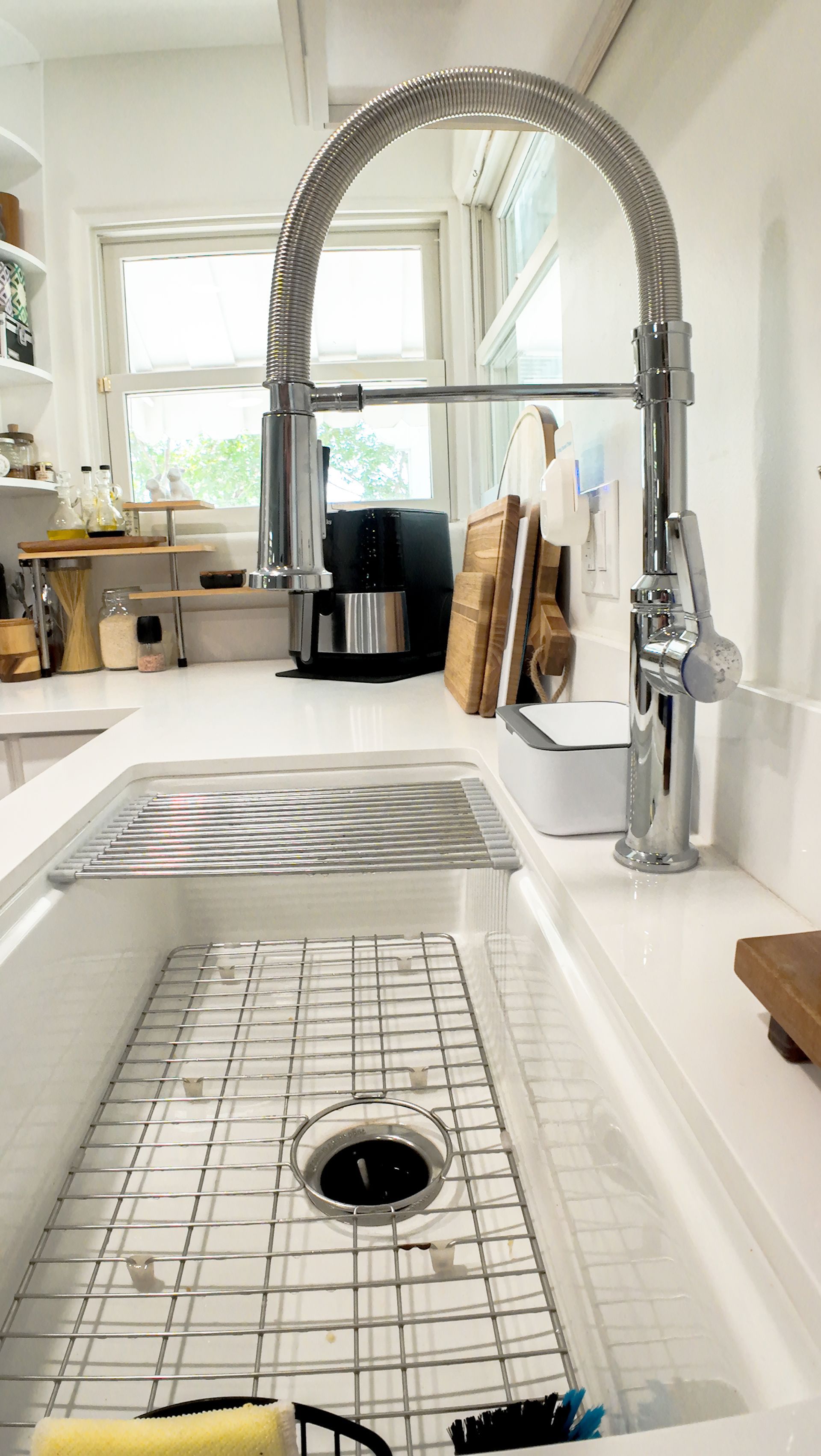 A white kitchen sink with a chrome faucet. A metal rack sits inside, and a window is in the background.