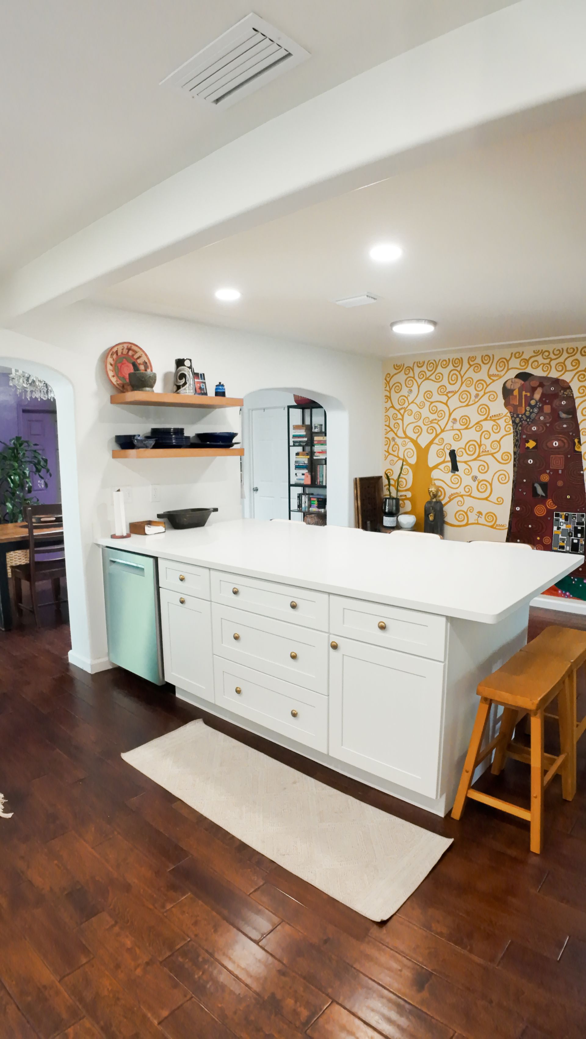 White kitchen with large island, wood floor, open shelves, and a mint-green dishwasher.