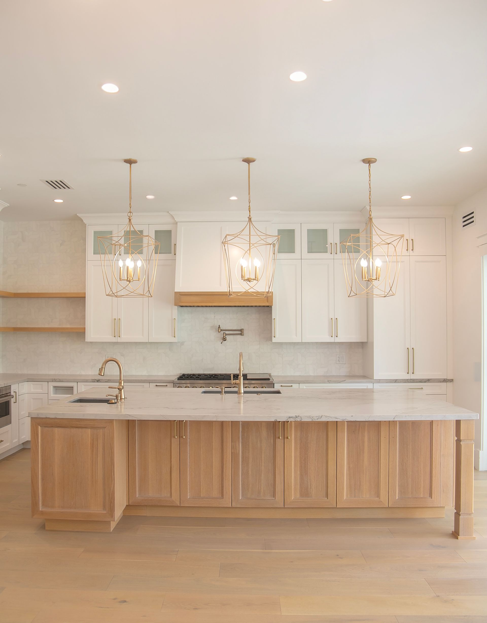 Modern kitchen with white upper cabinets, light wood island, and gold pendant lights.