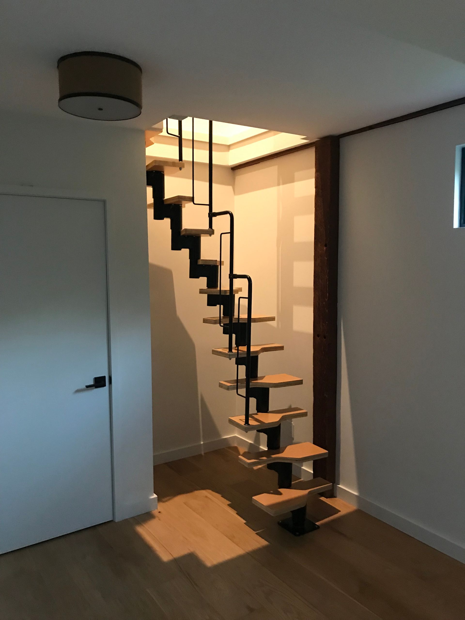 Modern open-tread staircase with wood steps and a black metal frame, set against a white wall in a residential interior.