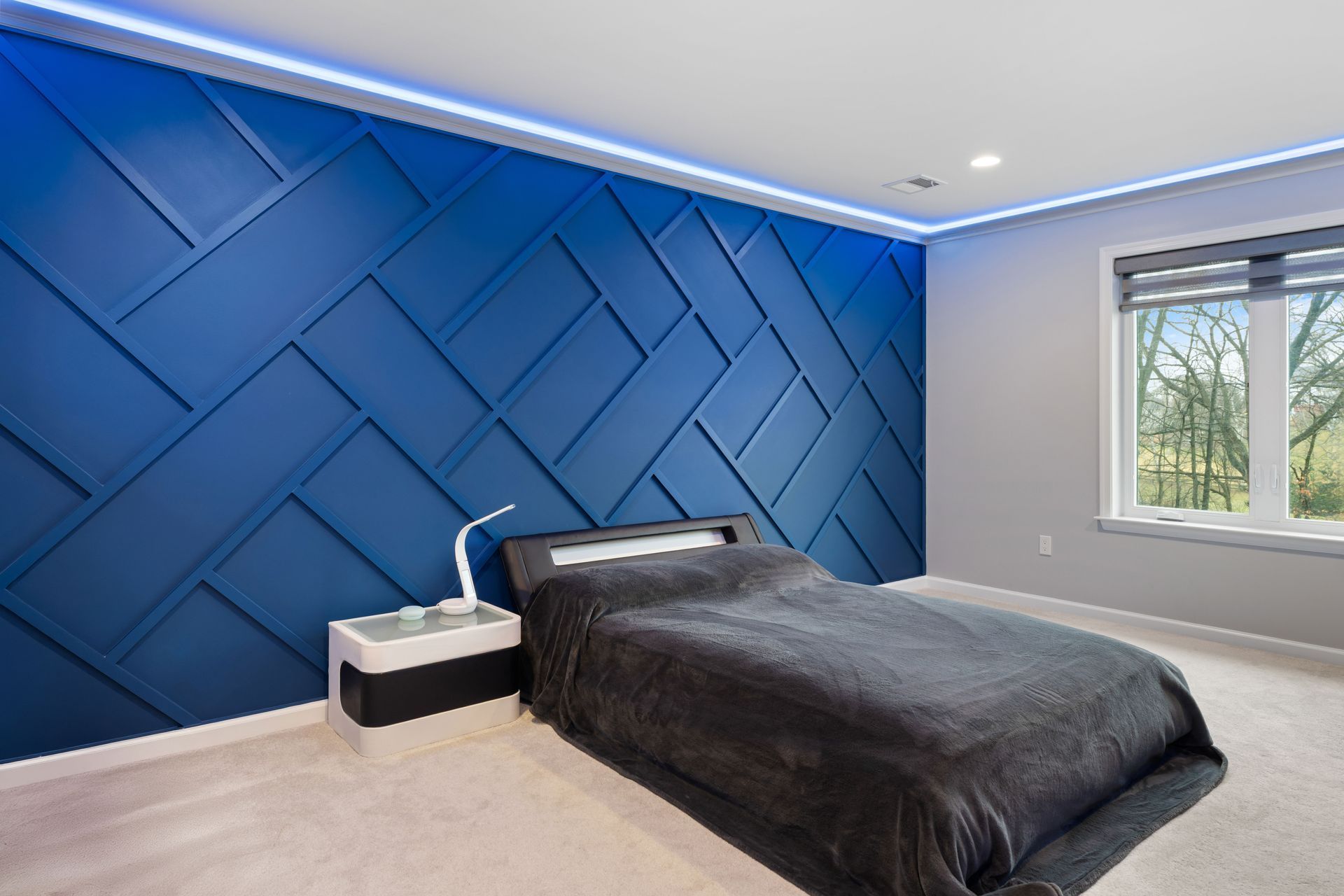 A bedroom featuring a blue accent wall with a geometric wood-panel pattern, a dark bed, and a modern white nightstand.