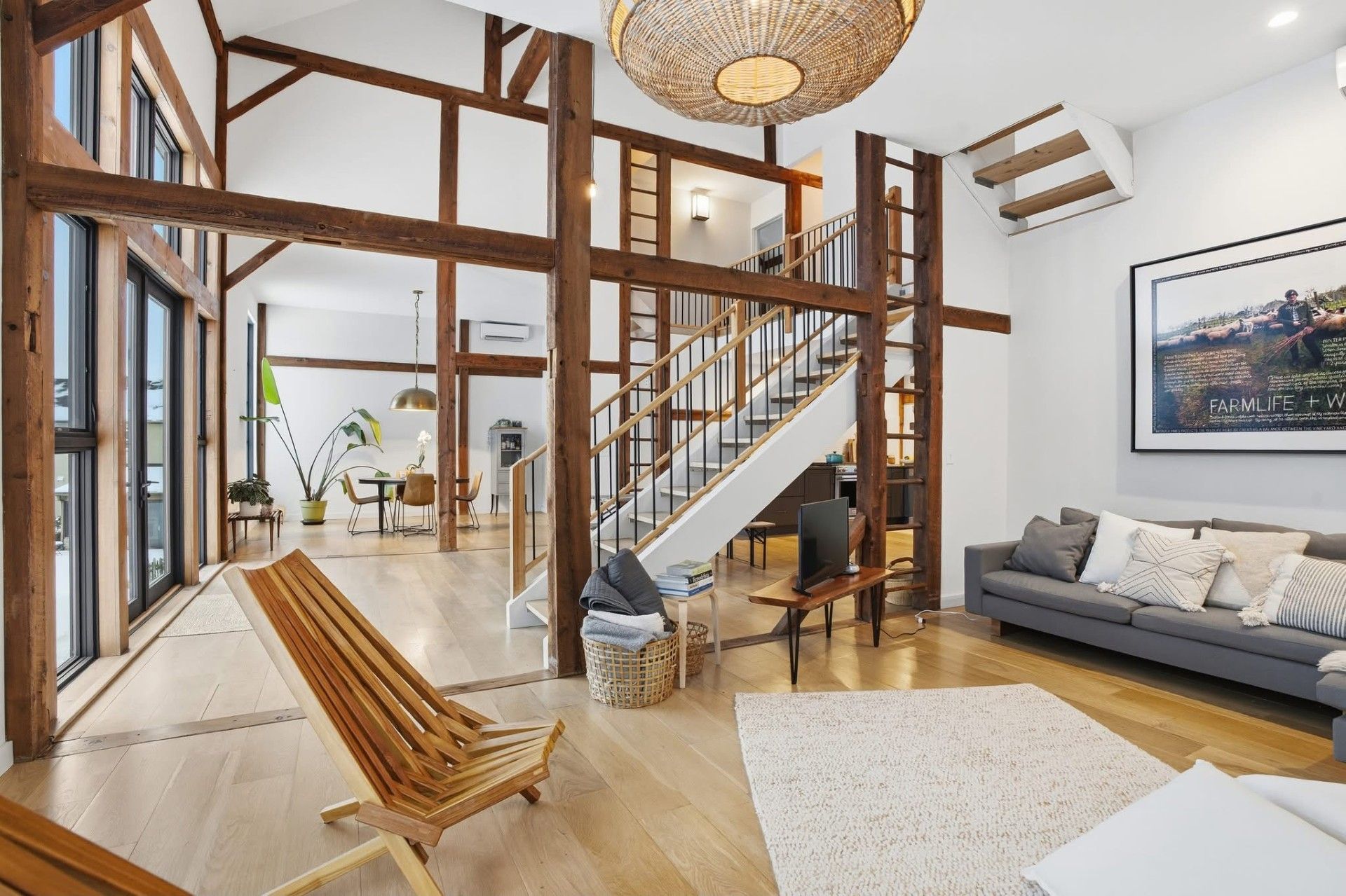 Spacious living room with exposed wooden beams, staircase, and modern furniture. Bright, natural light.