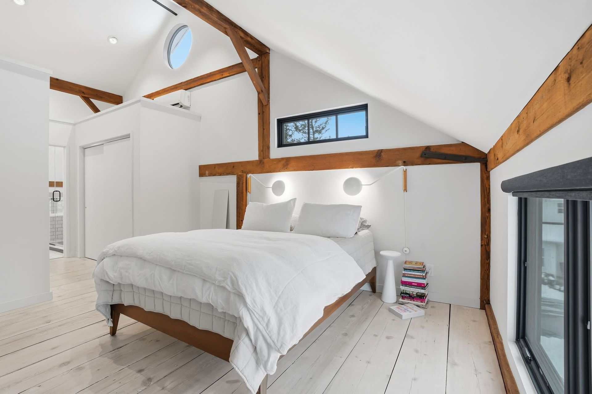 Bedroom with white walls and floors, exposed wood beams, and a bed.