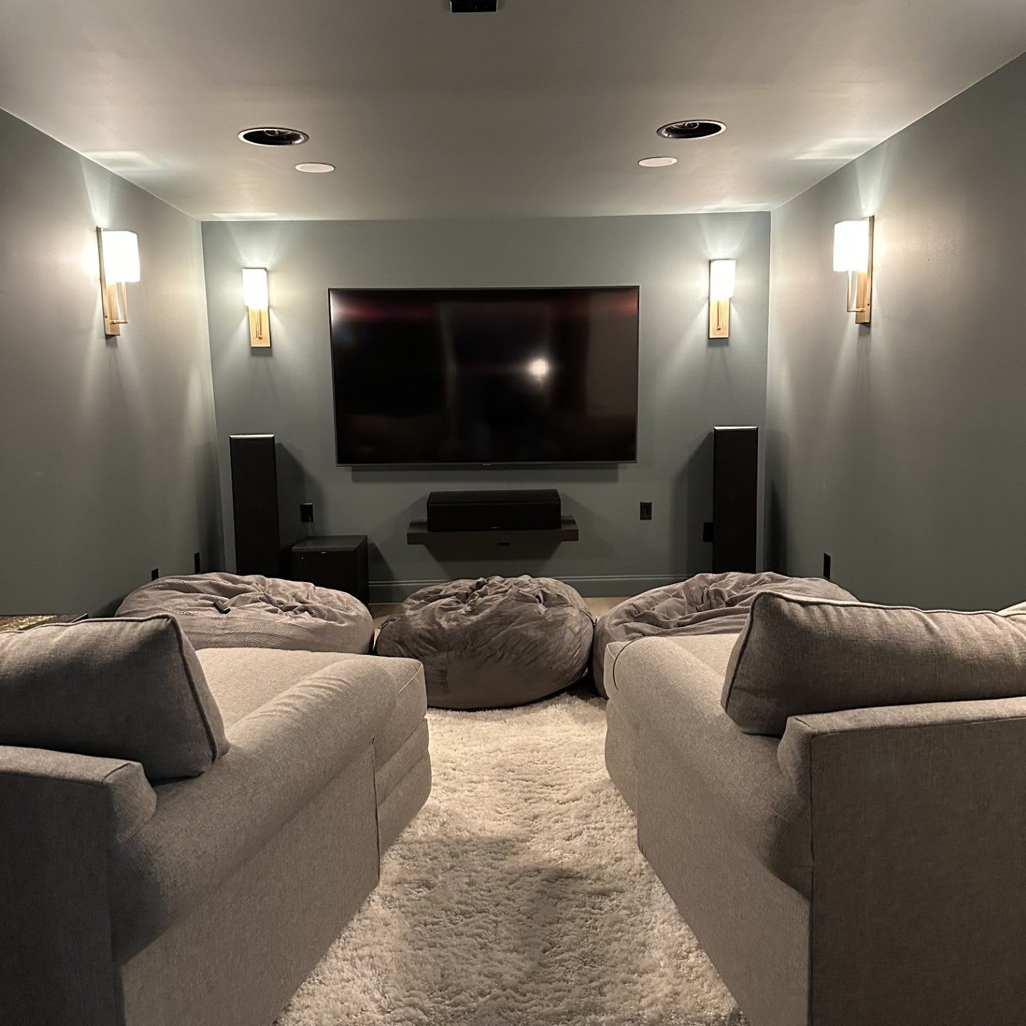 Home theater with TV, speakers, couches, bean bags, and wall sconces.