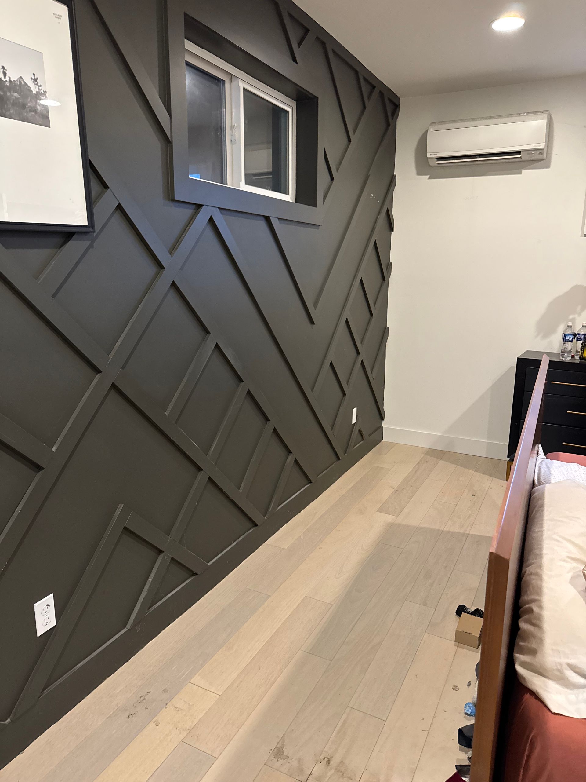Dark gray accent wall with geometric wood trim, small window, and light wood floor.