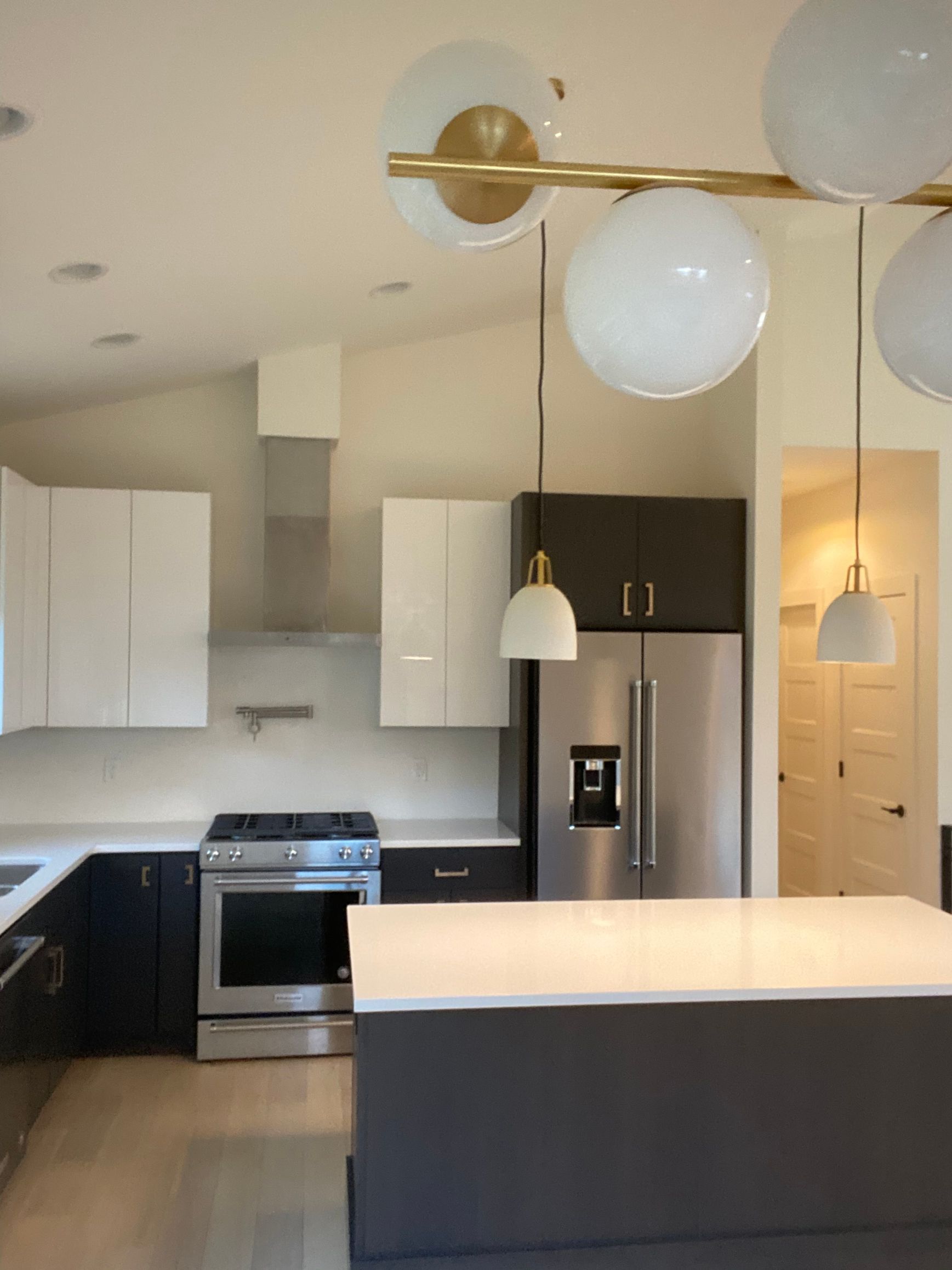 Modern kitchen with white and dark gray cabinets, stainless steel appliances, and large globe light fixture.