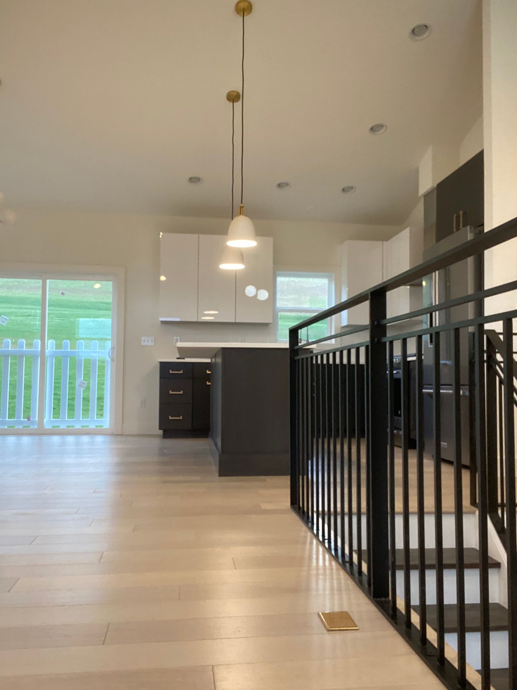 Modern kitchen with white cabinets, dark island, wood floor, and black railing.