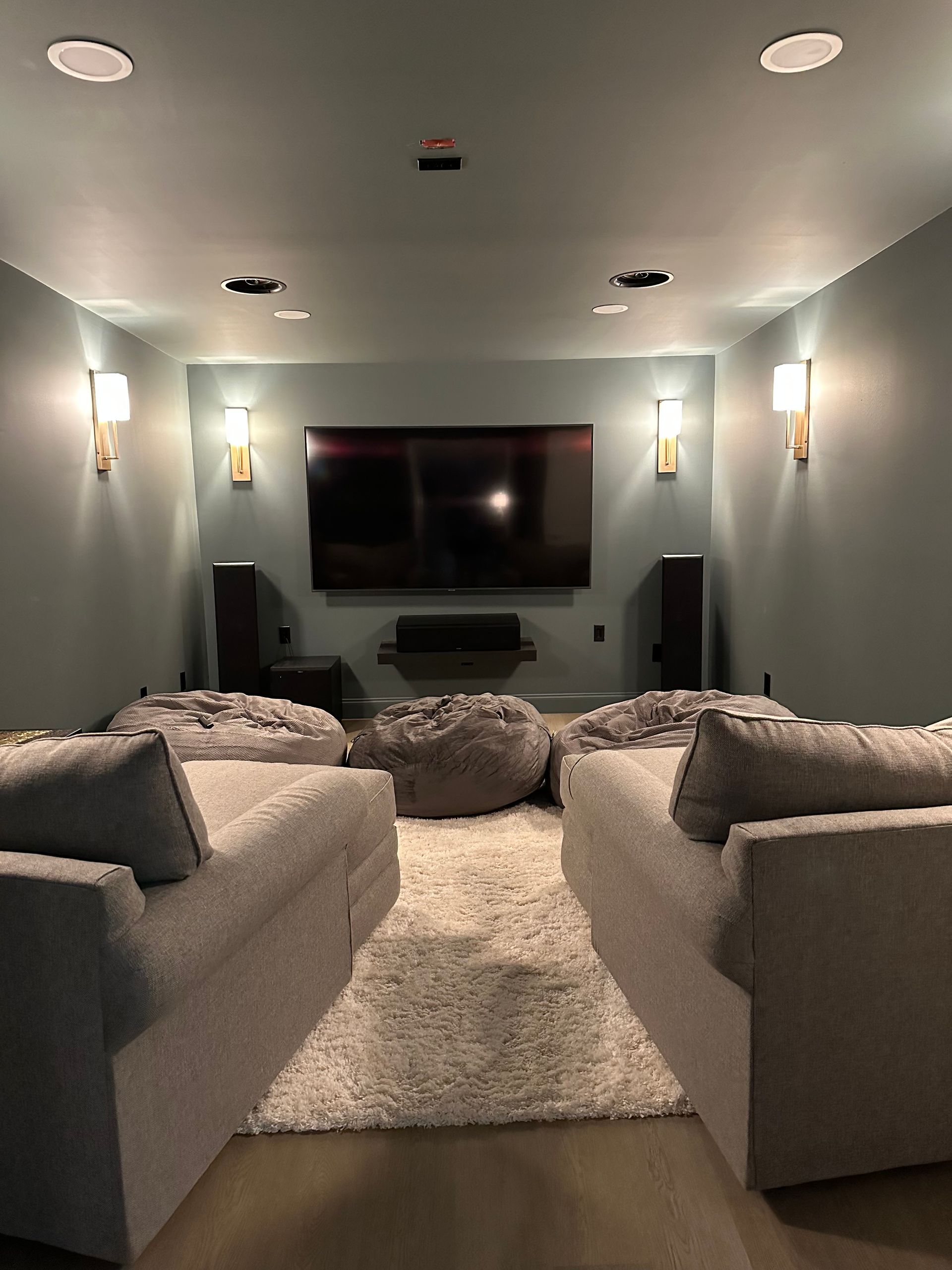 Home theater with blue walls, large screen, light-colored seating, rug, and wall sconces.