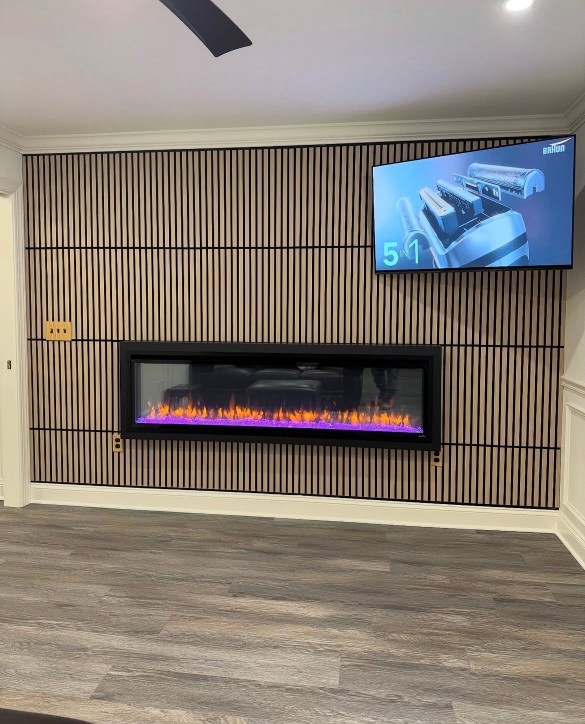 Fireplace with purple flames and a TV on a slat wood accent wall.