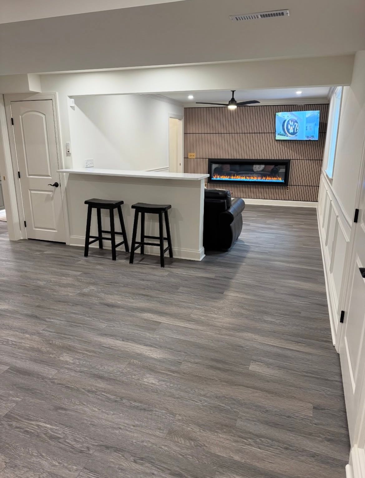 Basement with bar, stools, fireplace, TV, and wood-paneled wall. Dark flooring and white trim.