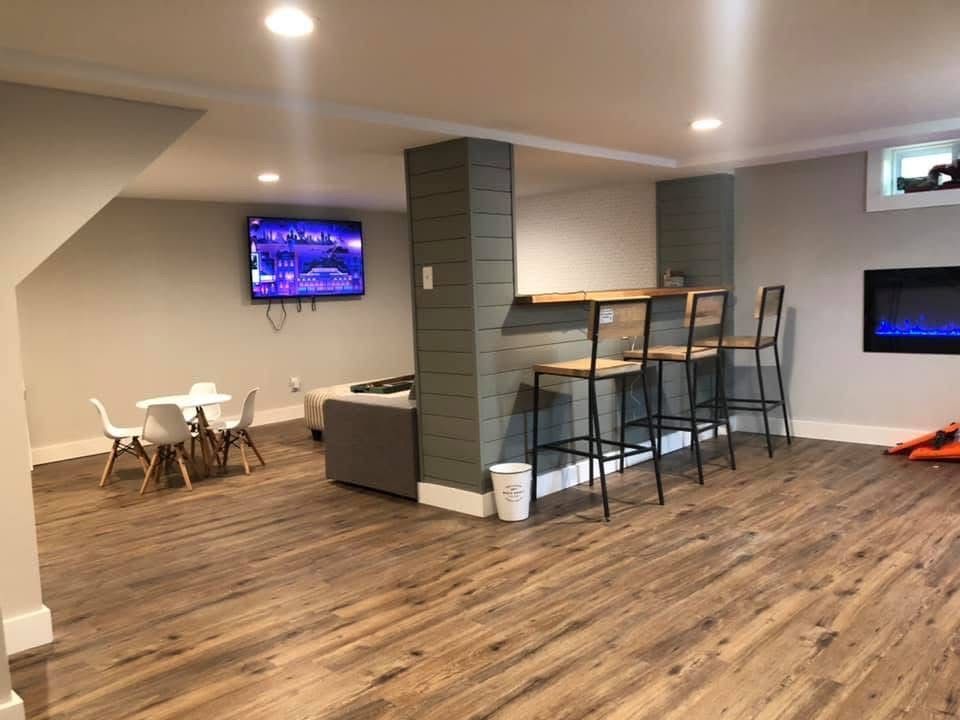 Finished basement with bar, small table with chairs, and fireplace. Wood-look flooring and gray walls.