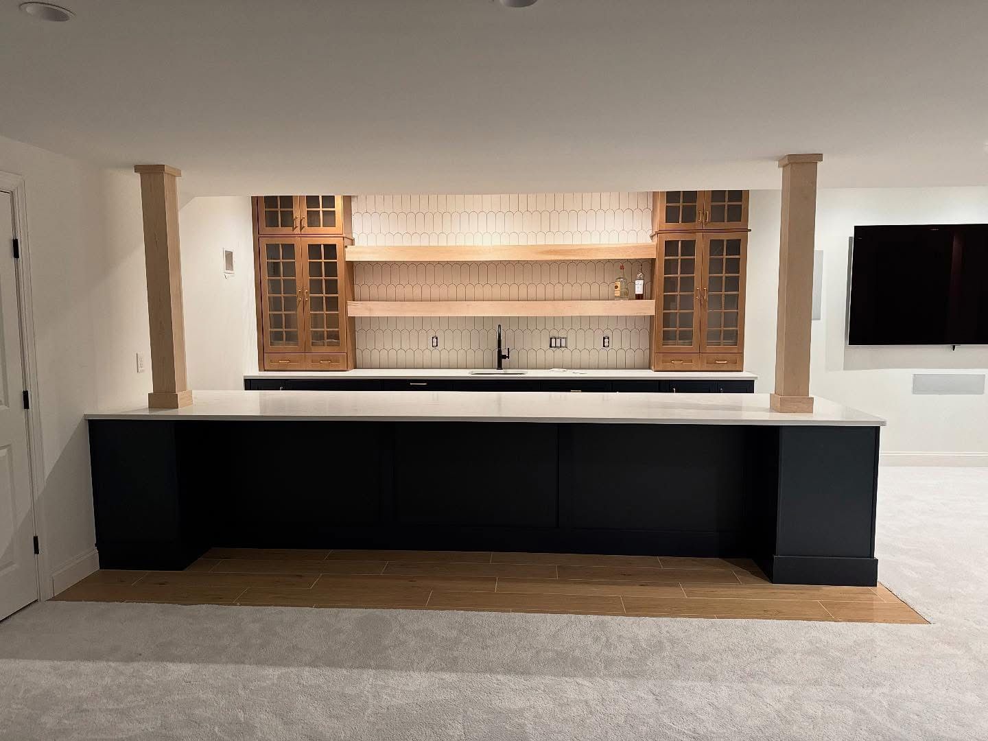A newly constructed home bar with a navy blue base, white countertop, and wood shelving.