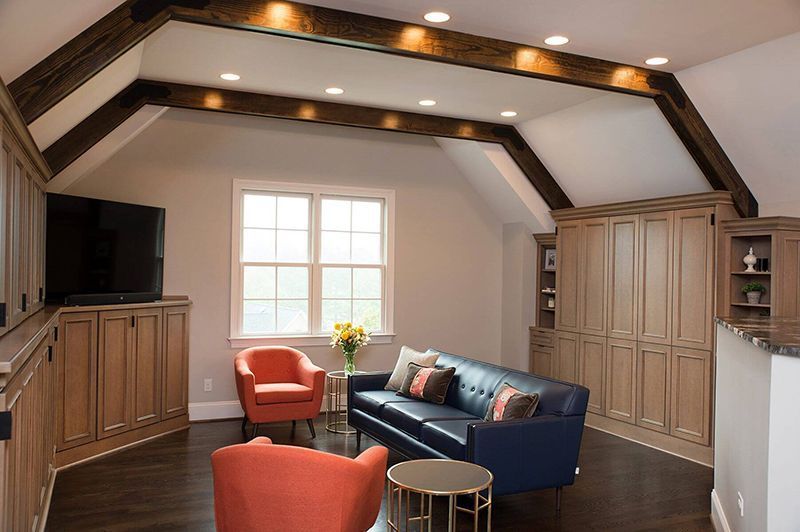 Living room with wooden beams, built-in cabinets, blue sofa, orange chairs, and a window.