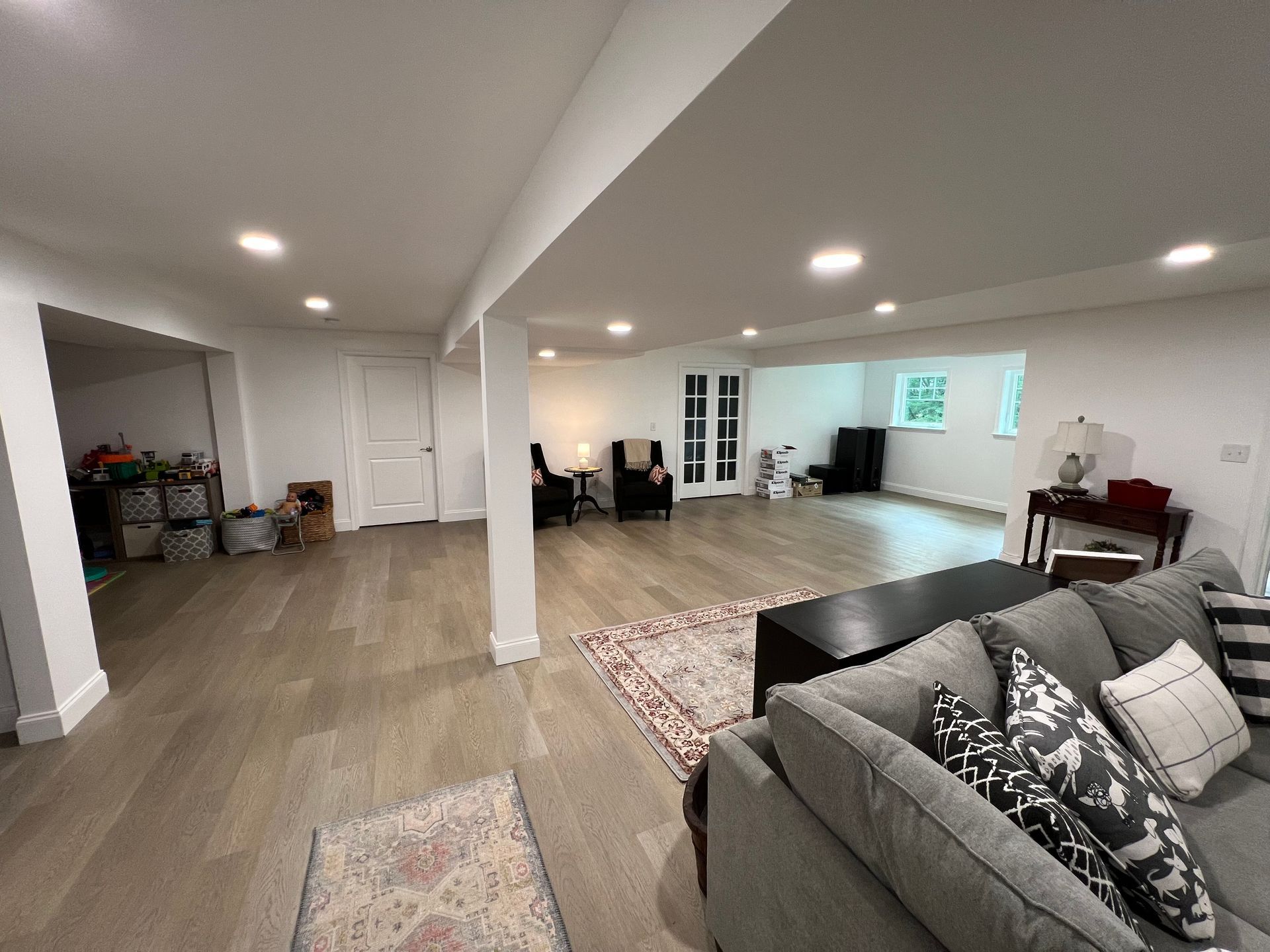 Spacious, bright basement living area with hardwood floors, white walls, and a gray sofa.