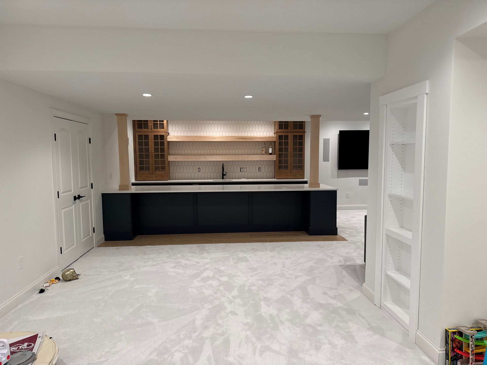 Basement bar with navy cabinets, light wood accents, and a white, textured backsplash.