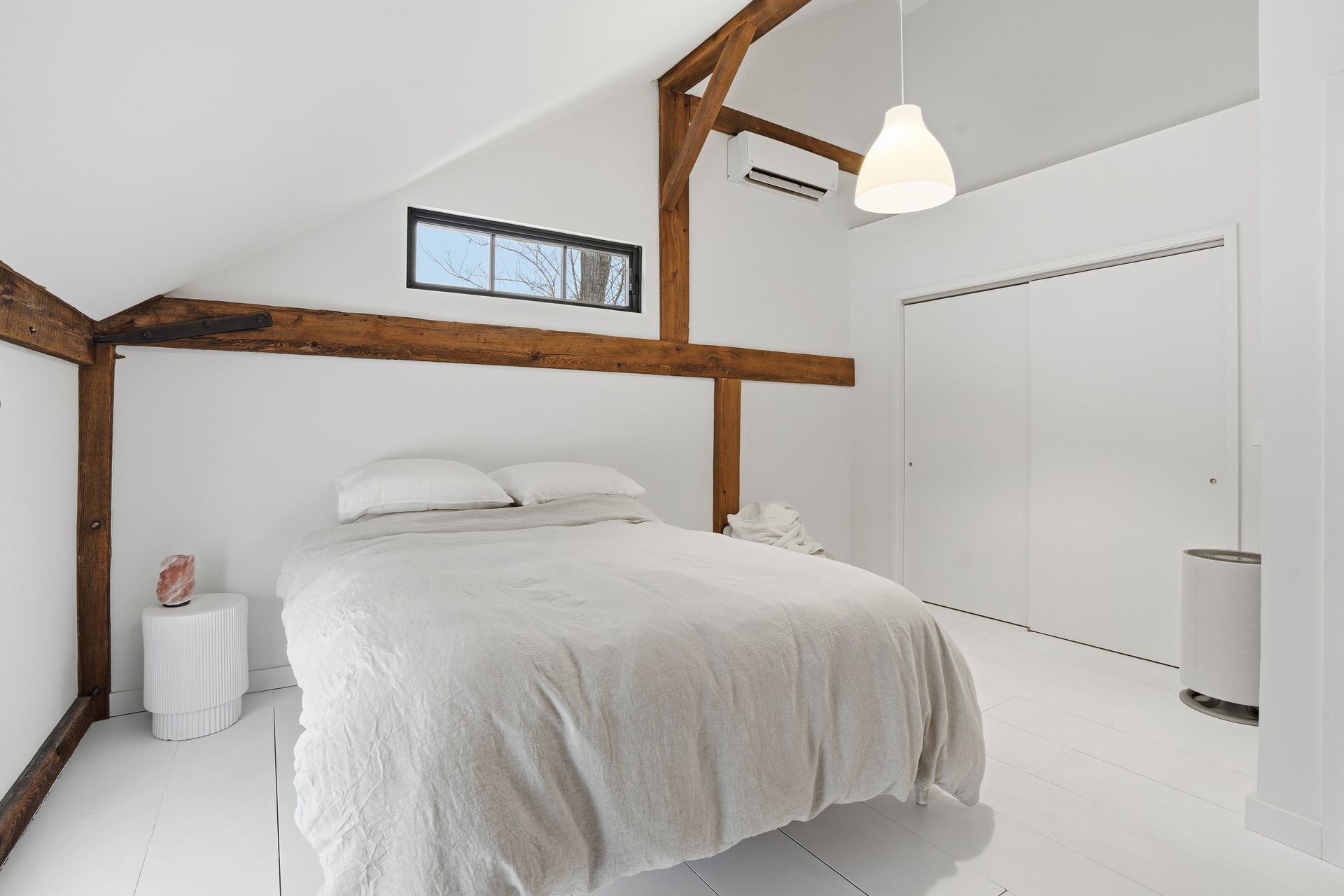 White bedroom with exposed wooden beams and a bed.