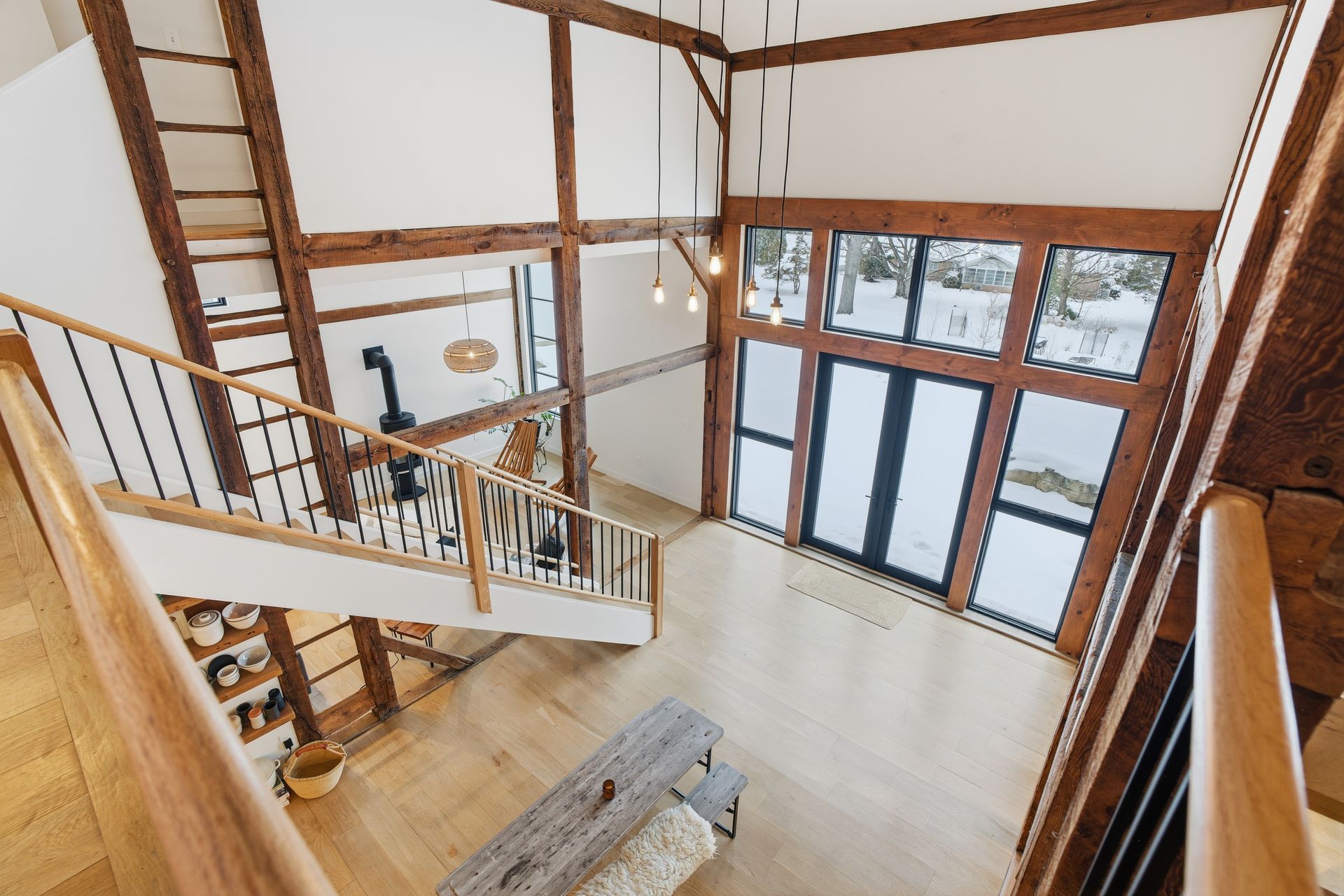 Wooden-framed interior with stairs, large windows, and a fireplace. Overhead view of a modern living space.