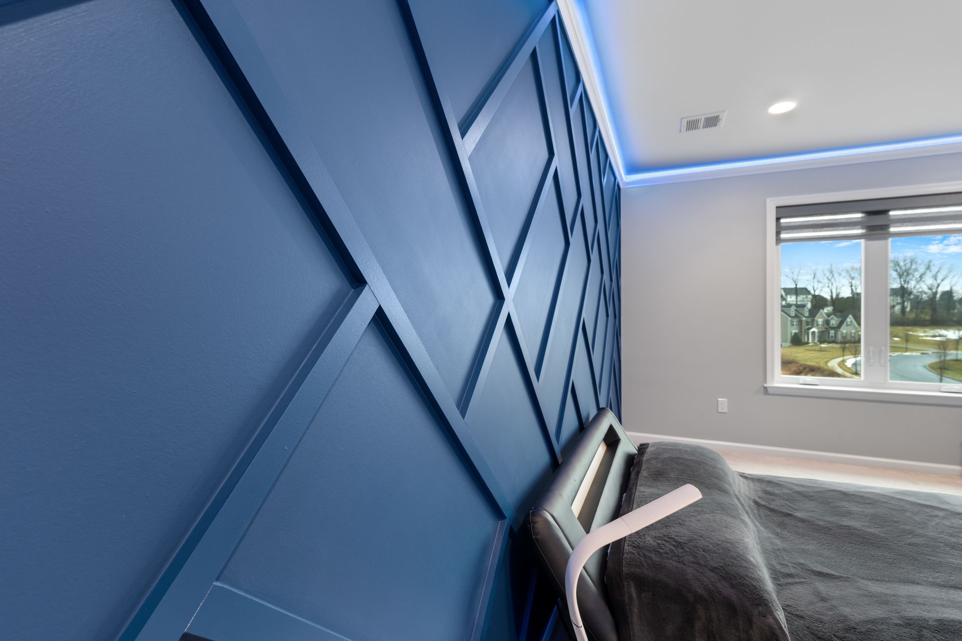 A blue, geometric-patterned accent wall in a bedroom with ambient cove lighting and a view of a neighborhood outside.