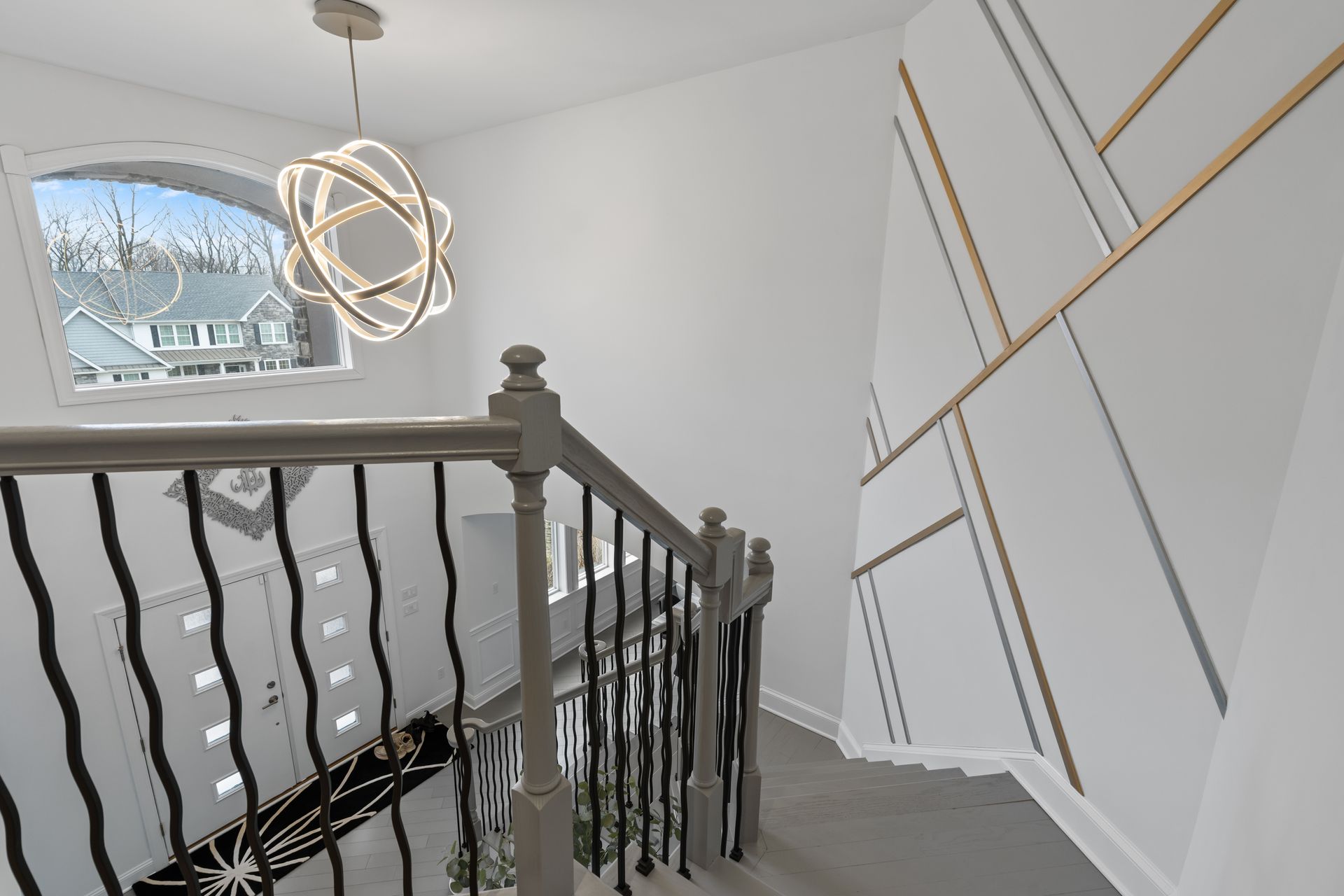 A staircase viewed from above, featuring a decorative wall with geometric wood trim and a modern orb chandelier overhead.