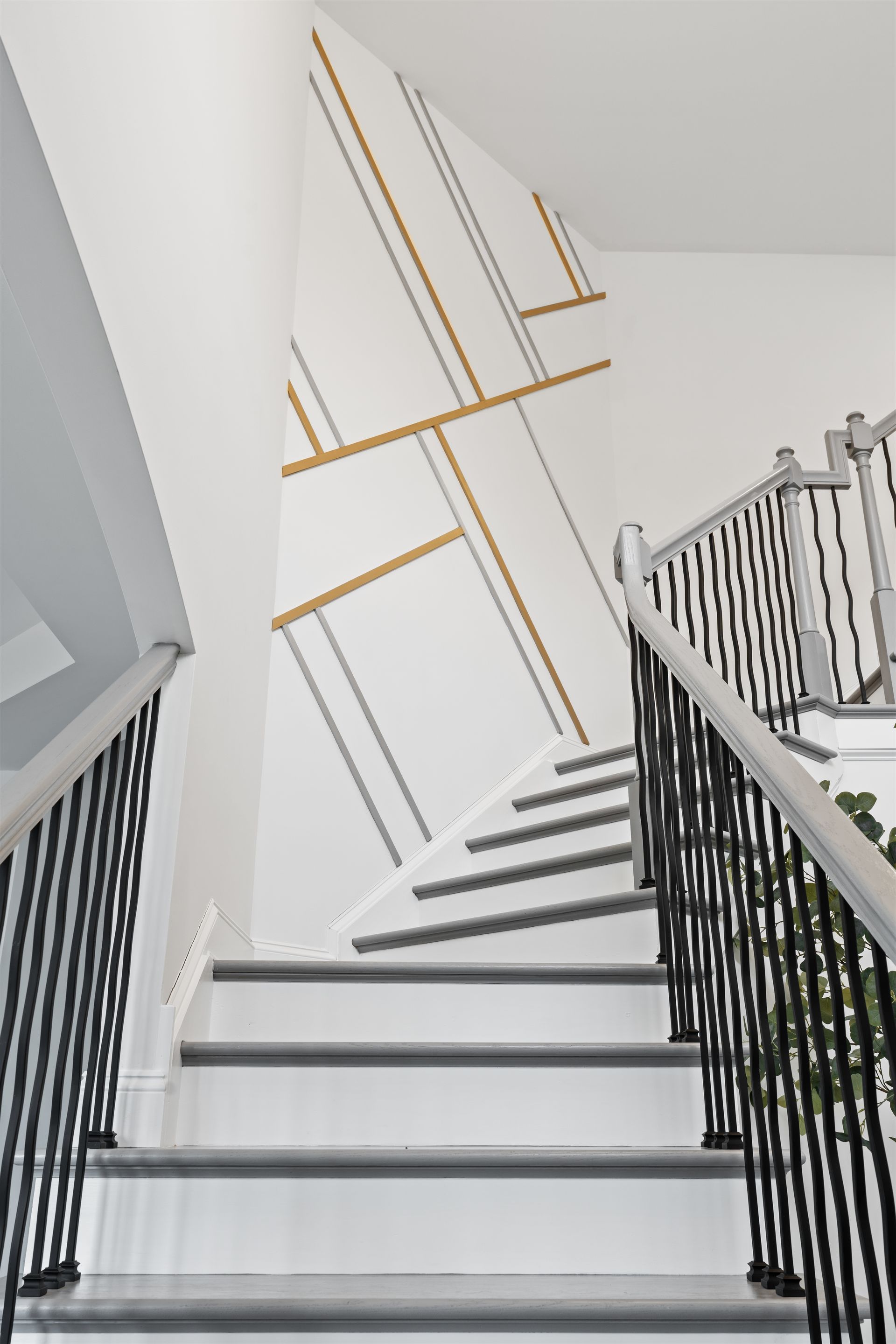 Staircase with white treads, dark metal railings, and a feature wall decorated with geometric gold and gray lines.