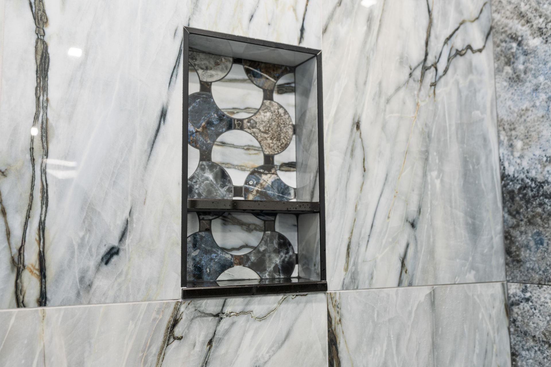 A built-in wall niche with circular patterned tile backings, set into a polished white marble wall.