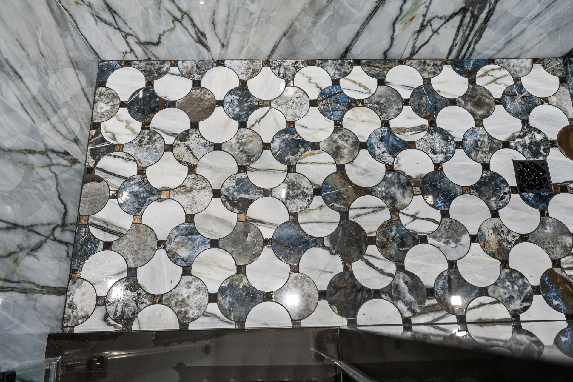 A shower floor with a decorative tile pattern featuring alternating white and dark marble circles connected by small squares.