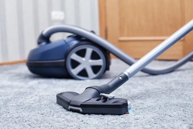 A blue vacuum cleaner sitting on a light gray carpet with the nozzle extended in the foreground.