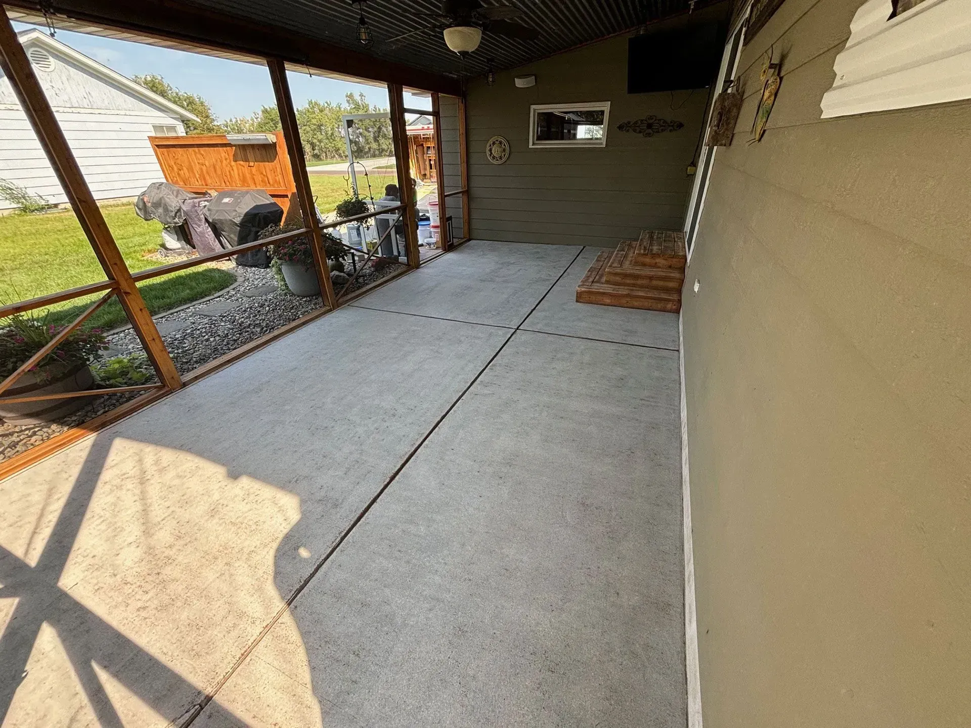 An empty screened-in porch with a concrete floor, wooden frame, and a view of a backyard.