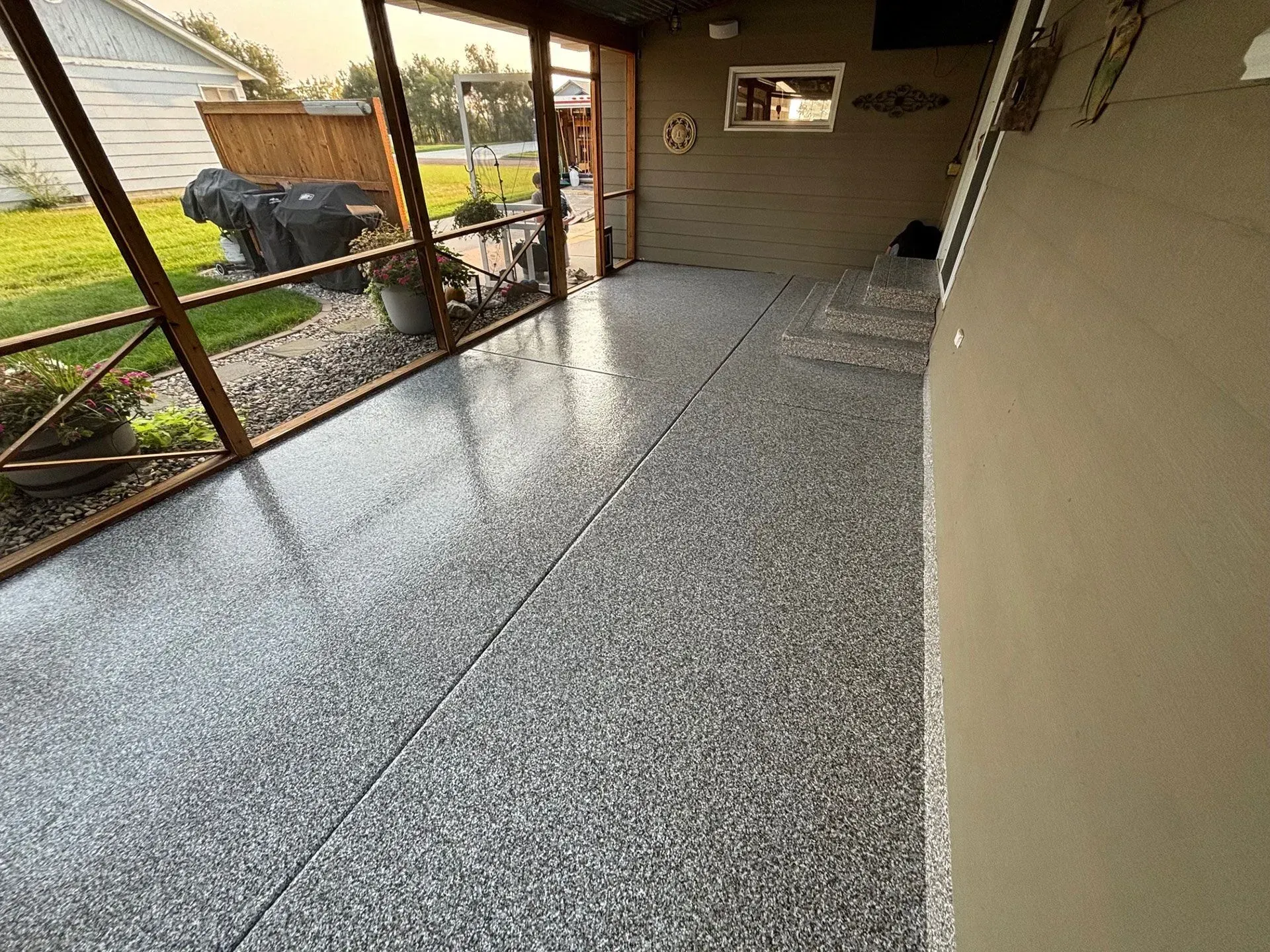 A screened-in porch with a glossy, grey granite-look epoxy floor, brown walls, and an outdoor view.