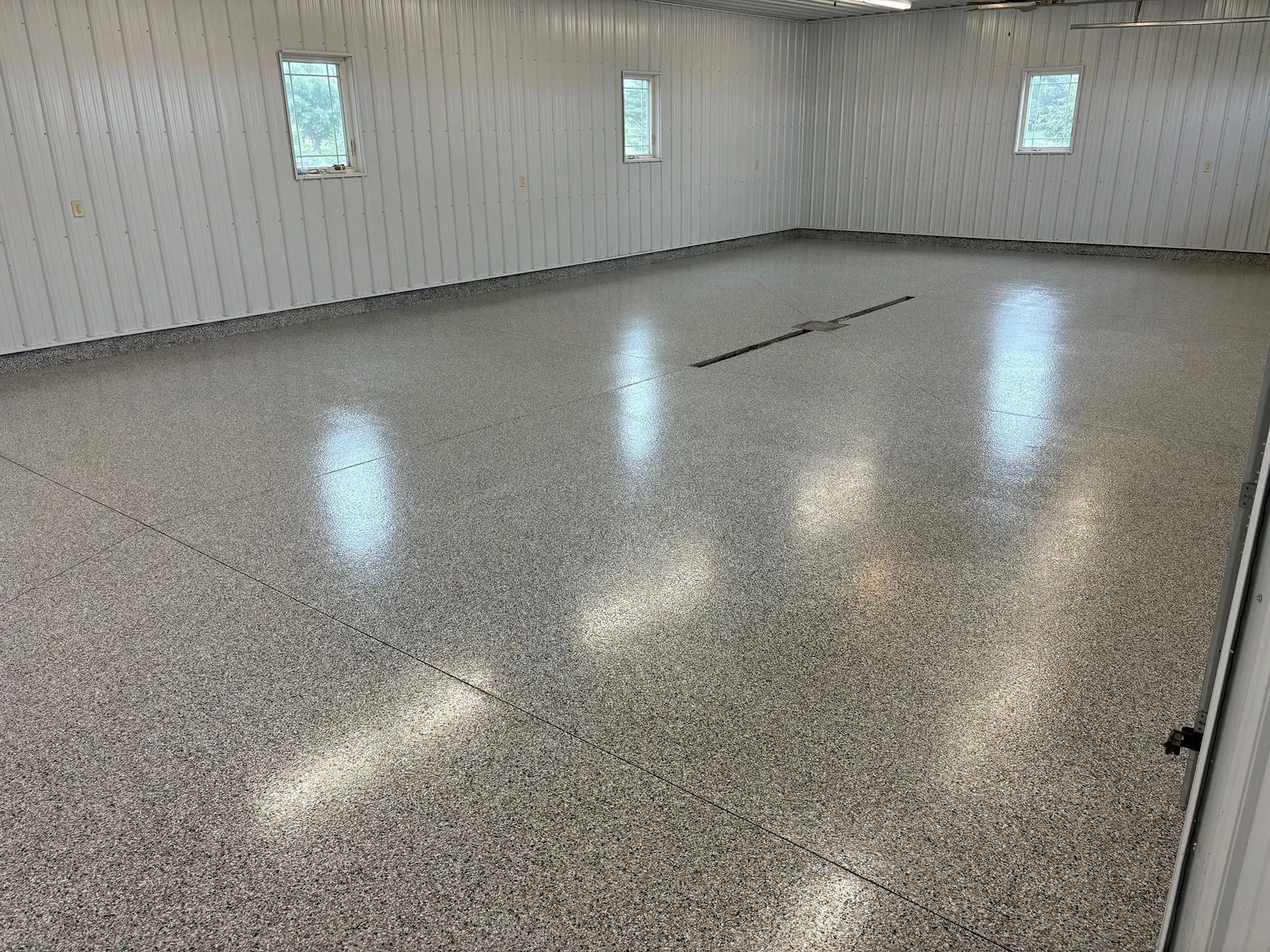 Empty garage interior with white corrugated walls, three small windows, and a grey speckled epoxy floor.