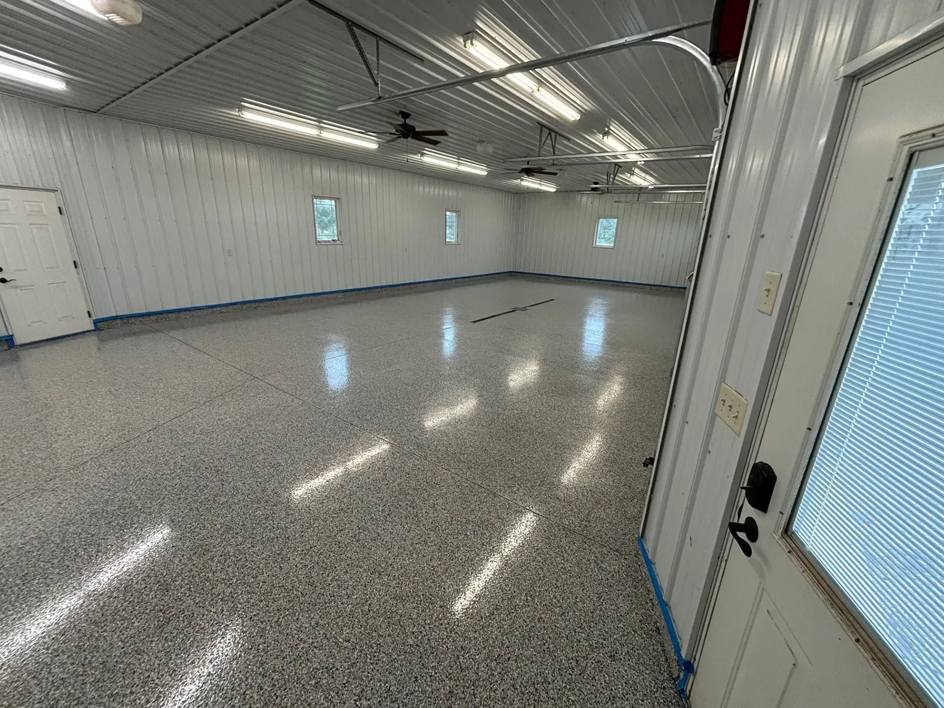 A bright, empty garage with white walls, a polished speckled gray epoxy floor, and overhead LED lights.