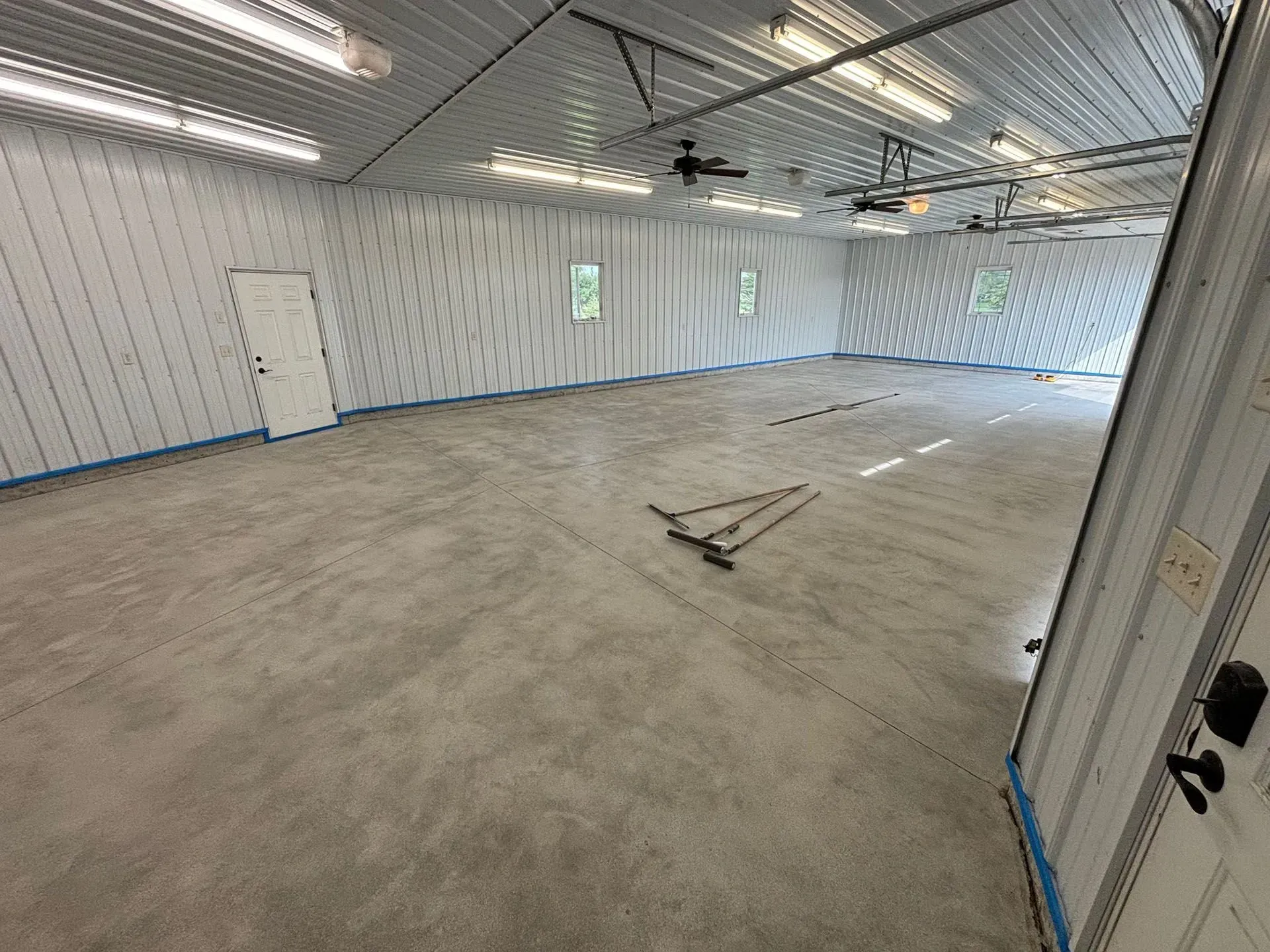 Empty, spacious indoor workshop with white corrugated walls, concrete flooring, and overhead lighting.
