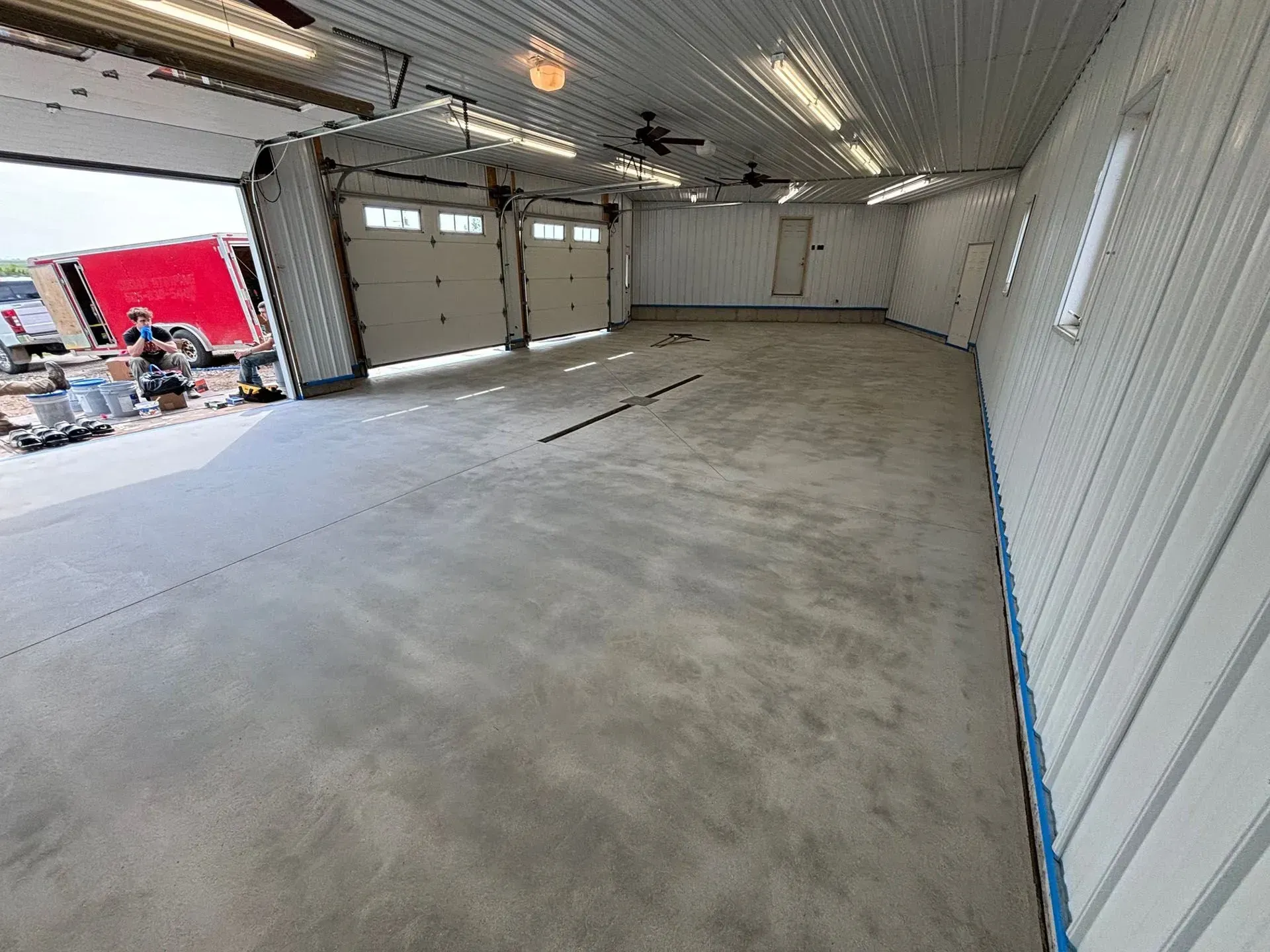 A spacious, empty garage with a polished concrete floor, white metal walls, and two closed garage doors.