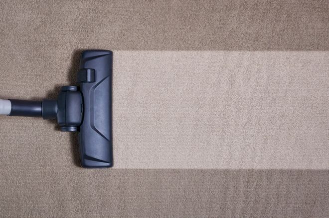 A vacuum cleaner head cleans a path across a brown carpet, revealing a lighter beige color underneath.