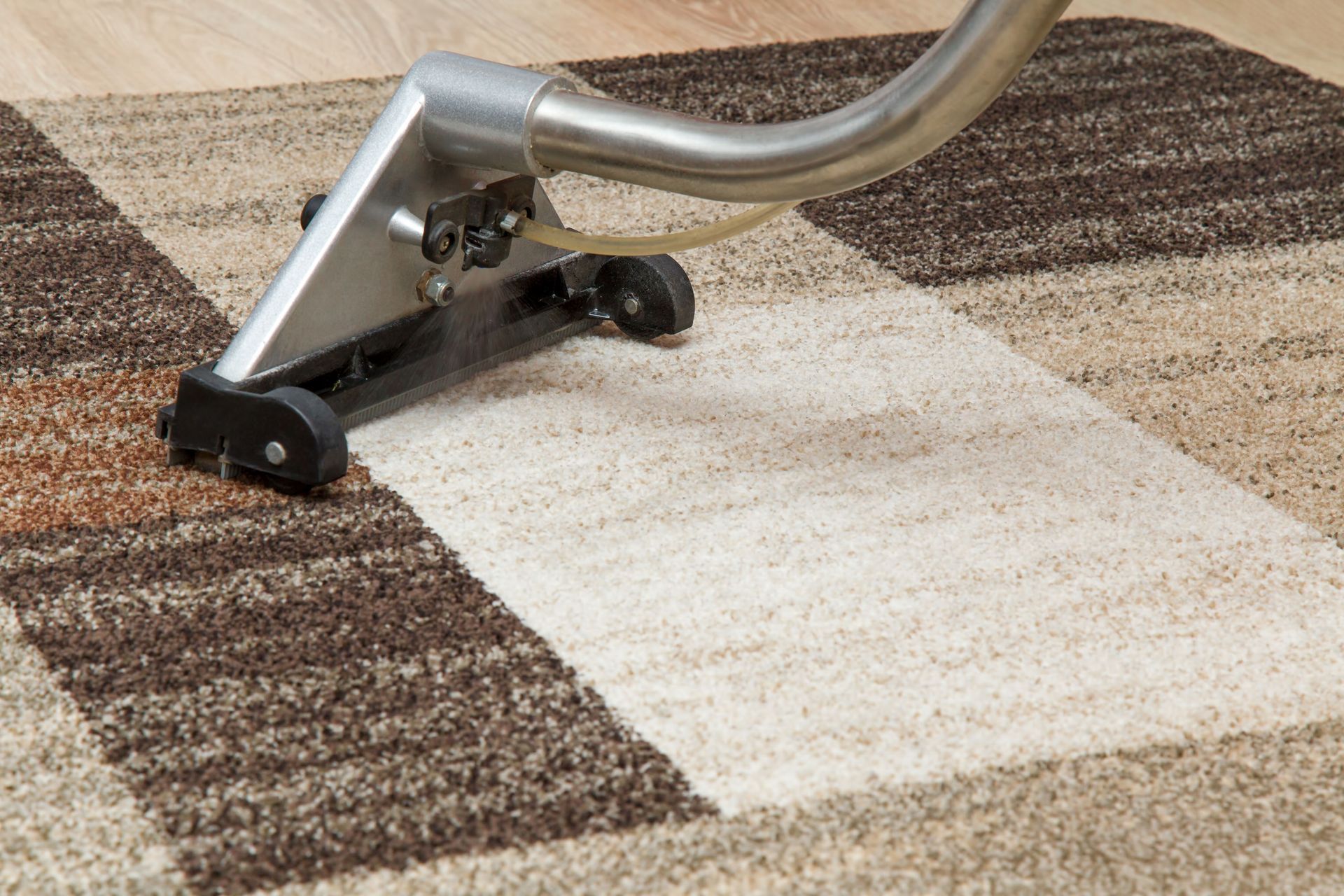 A metal carpet cleaner wand cleaning a section of a multi-colored brown and cream patterned area rug.