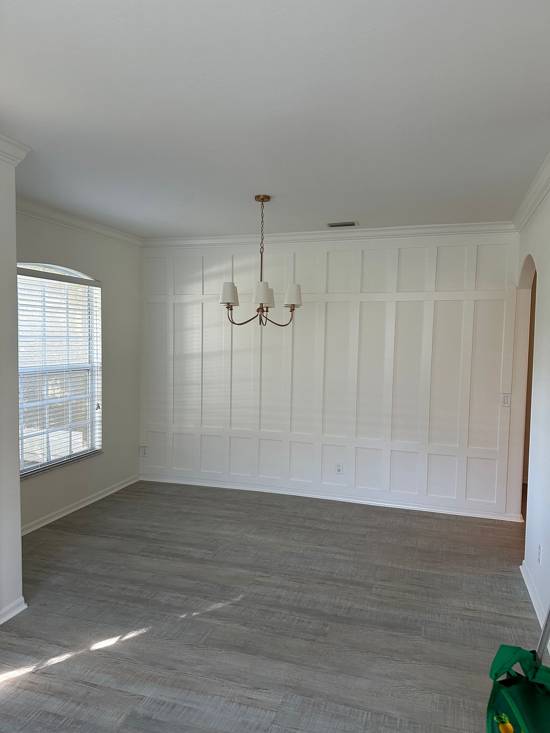 An empty living room with white walls and a chandelier hanging from the ceiling.