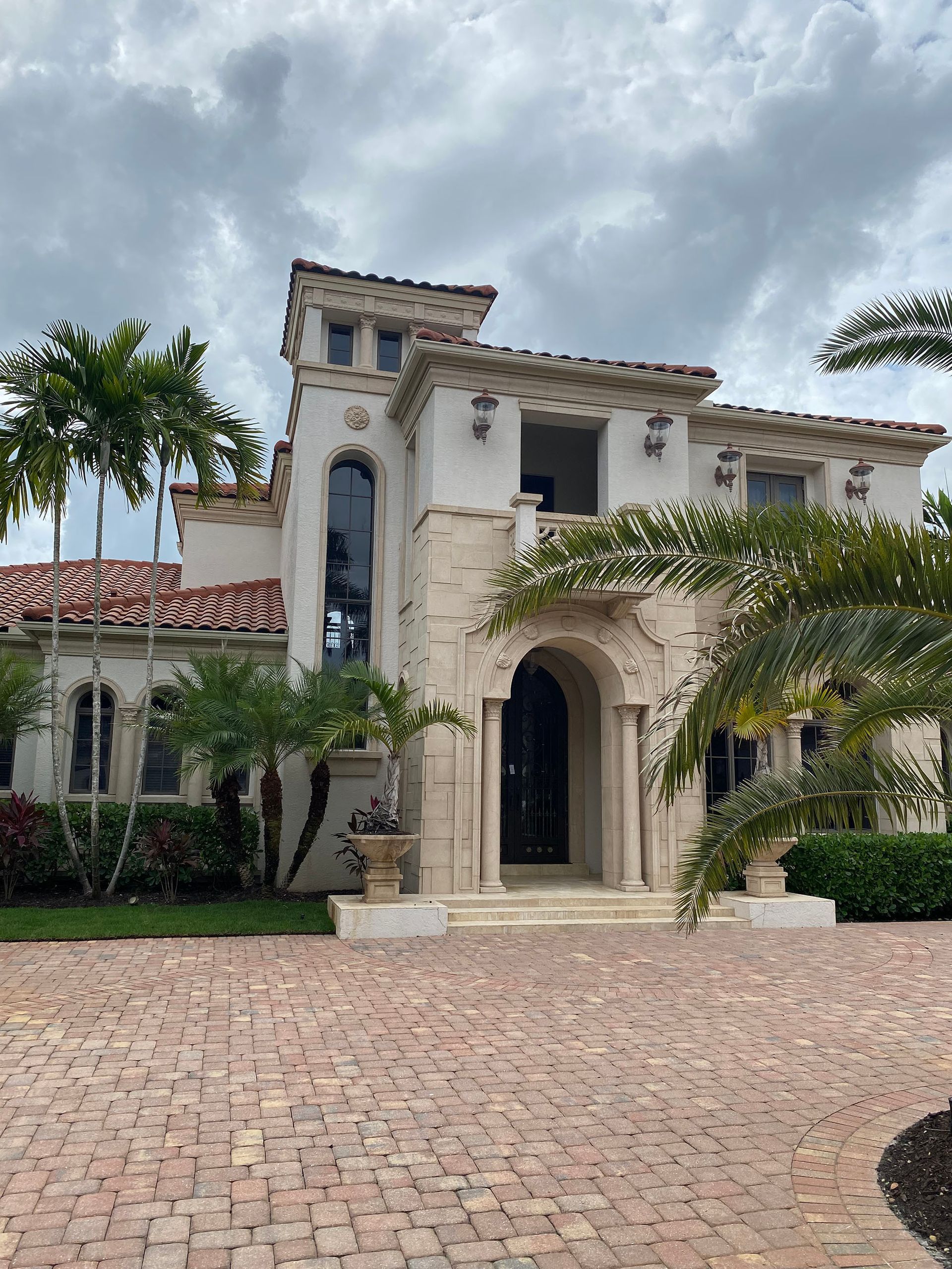 A large house with a brick driveway and palm trees in front of it