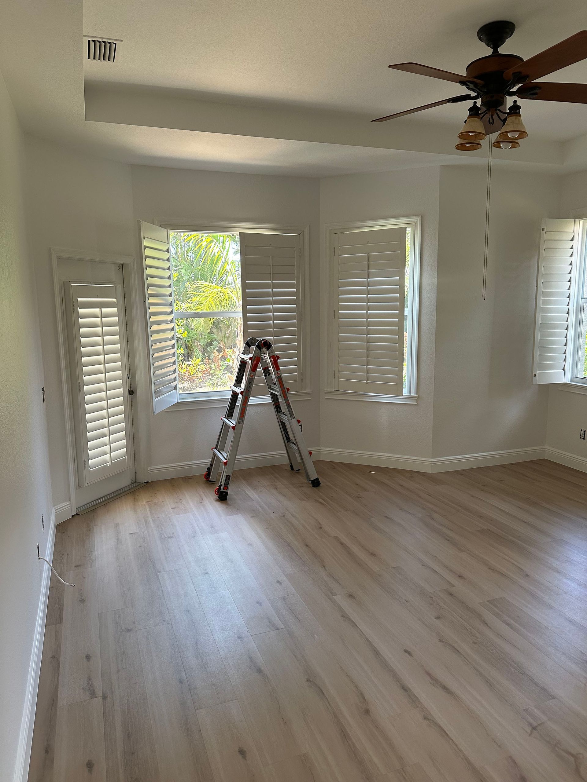 There is a ladder in the middle of the room with a ceiling fan.