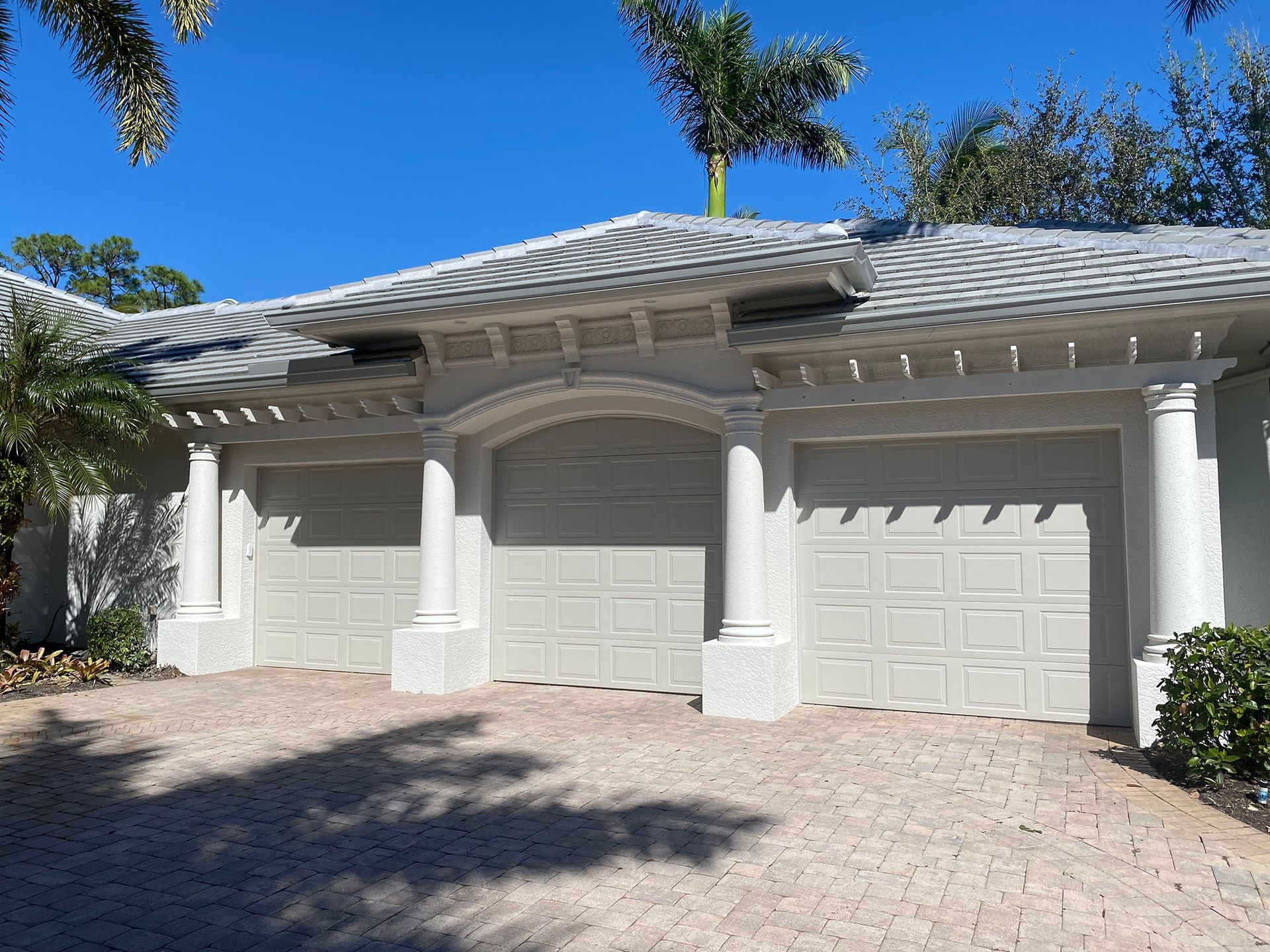 A white house with three garage doors and palm trees in the background