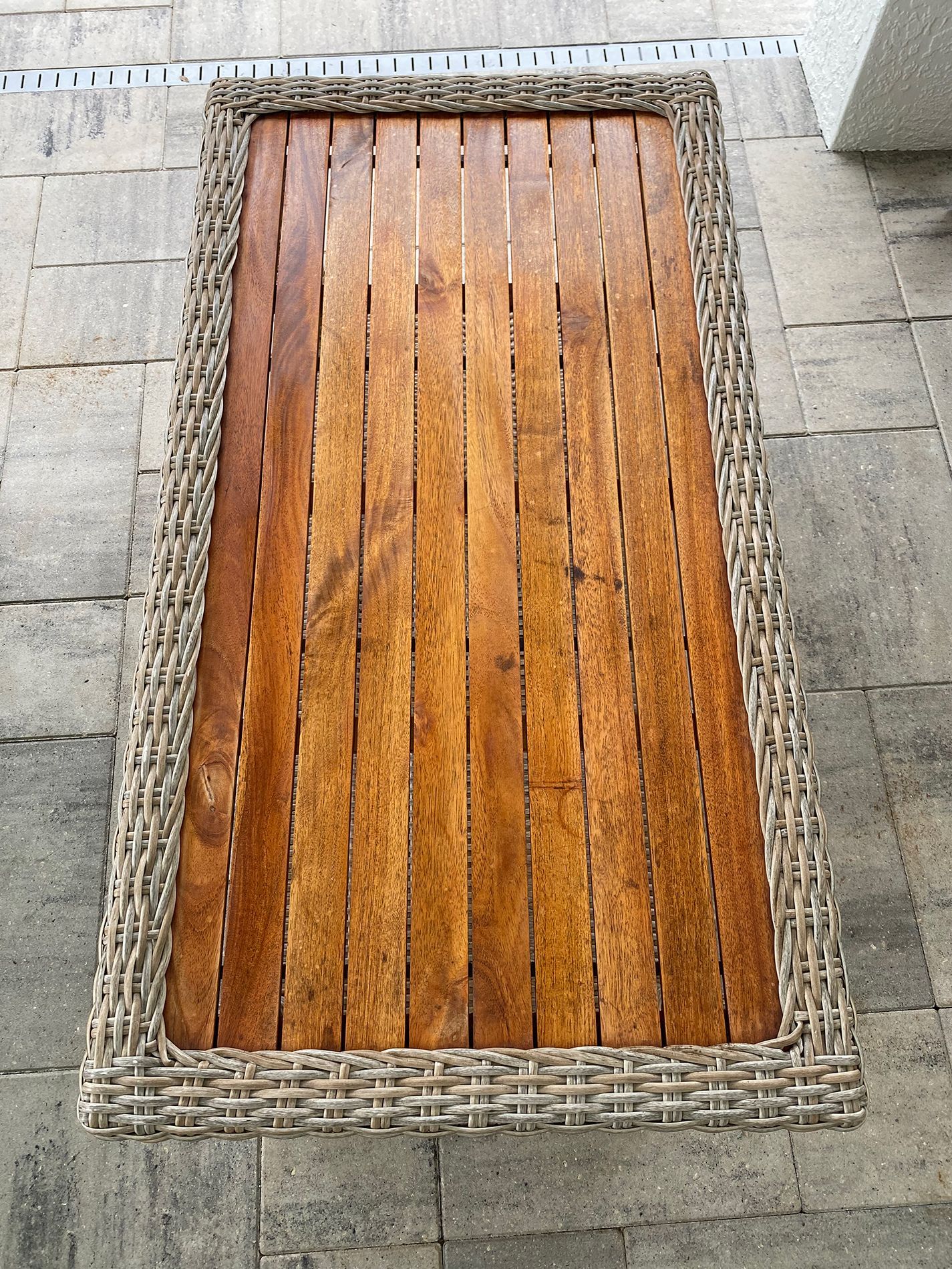 A wicker table with a wooden top sits on a brick floor
