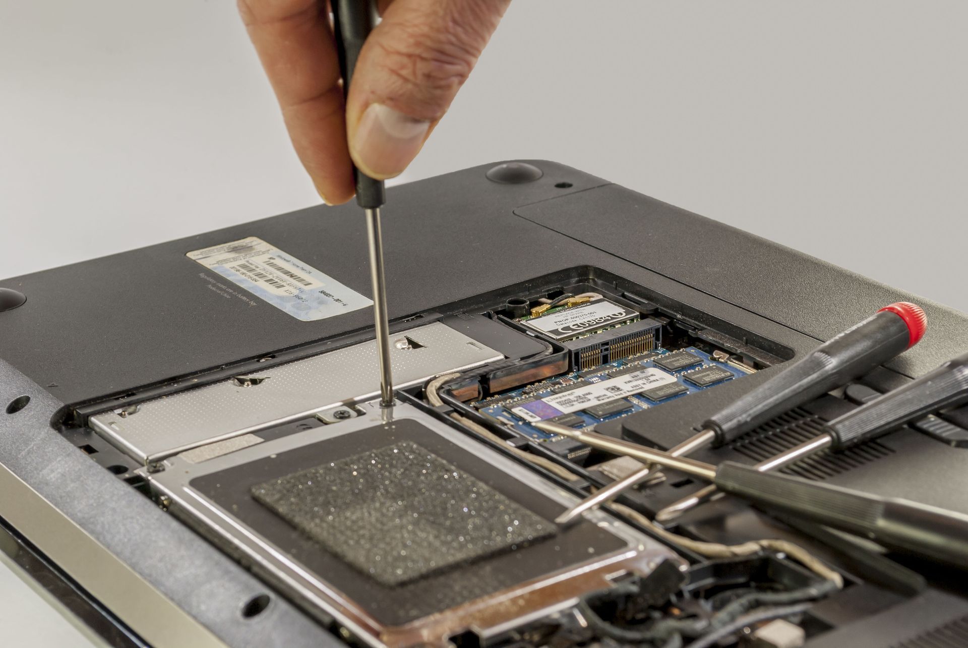 Hand using a screwdriver to open a laptop, exposing internal components and battery.