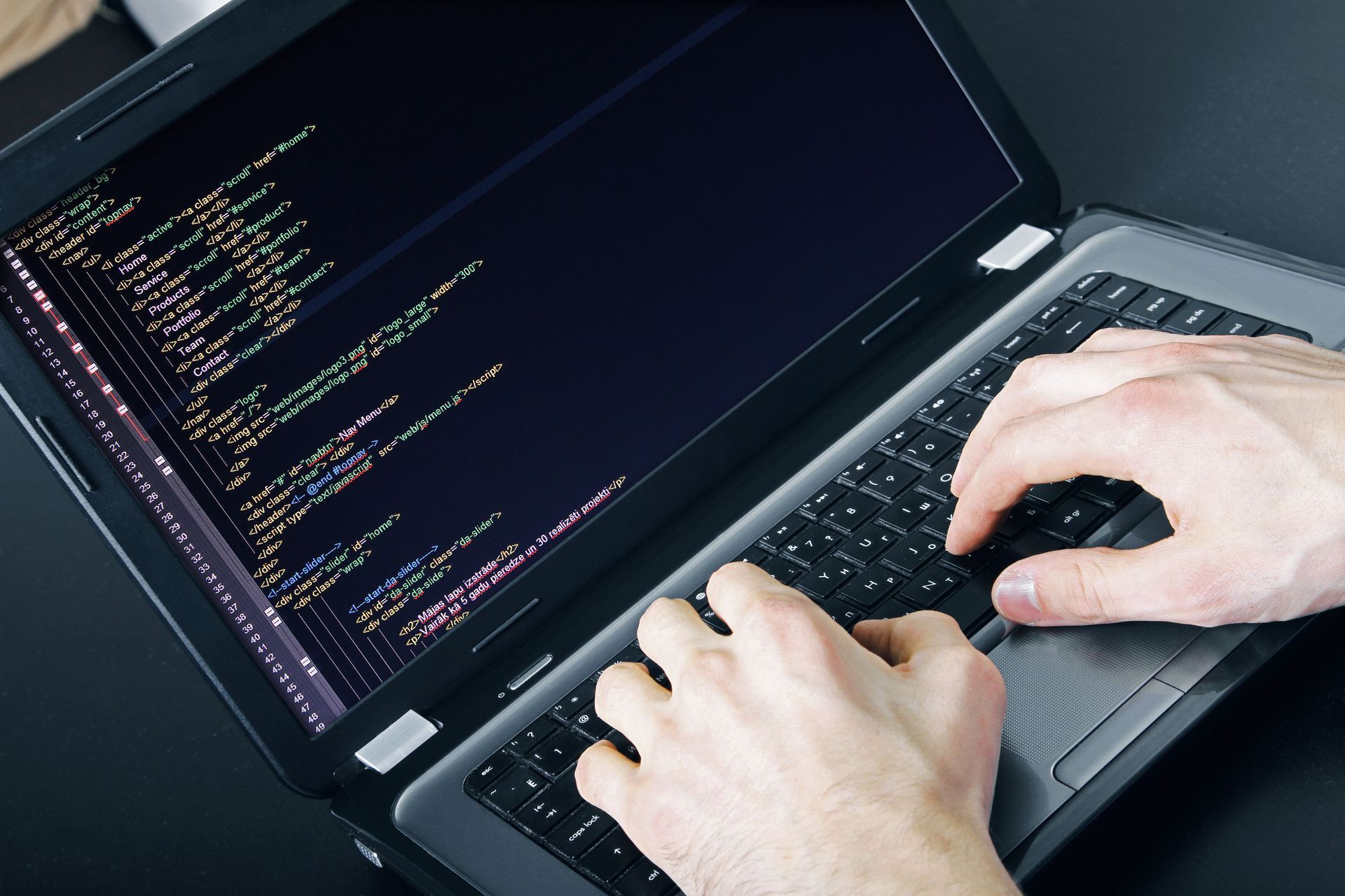 Hands typing on a laptop displaying code on a dark screen