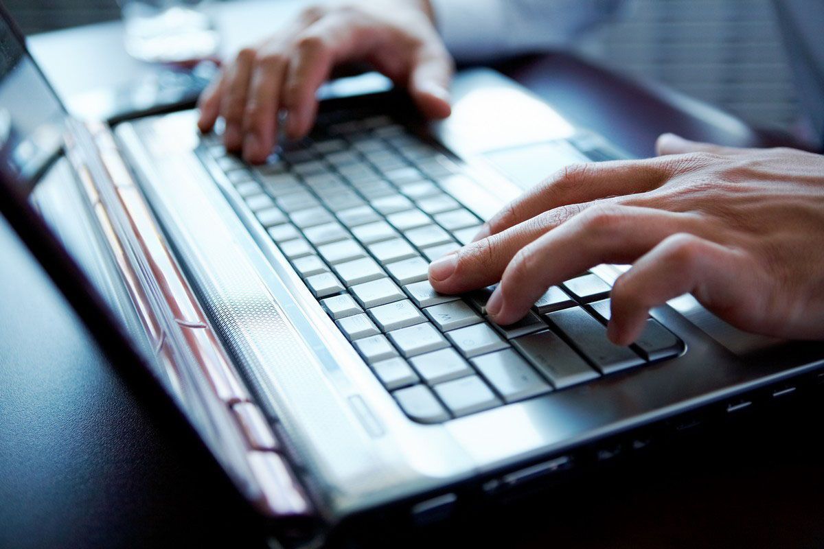 Hands typing on a laptop keyboard, close-up in cool blue light.