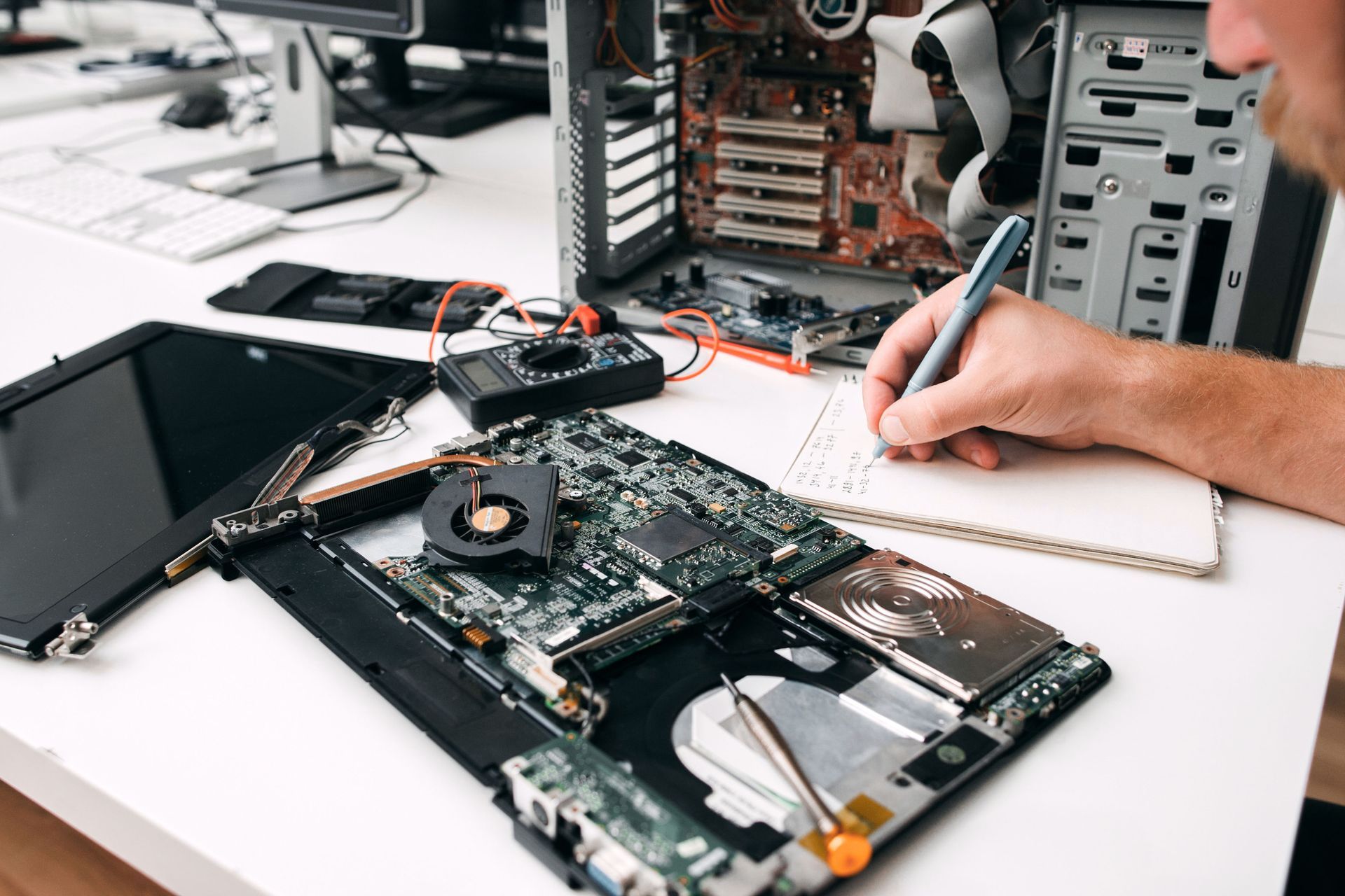 Laptop being repaired on a workbench, with tools, exposed circuit boards, and a hand using a screwdriver.