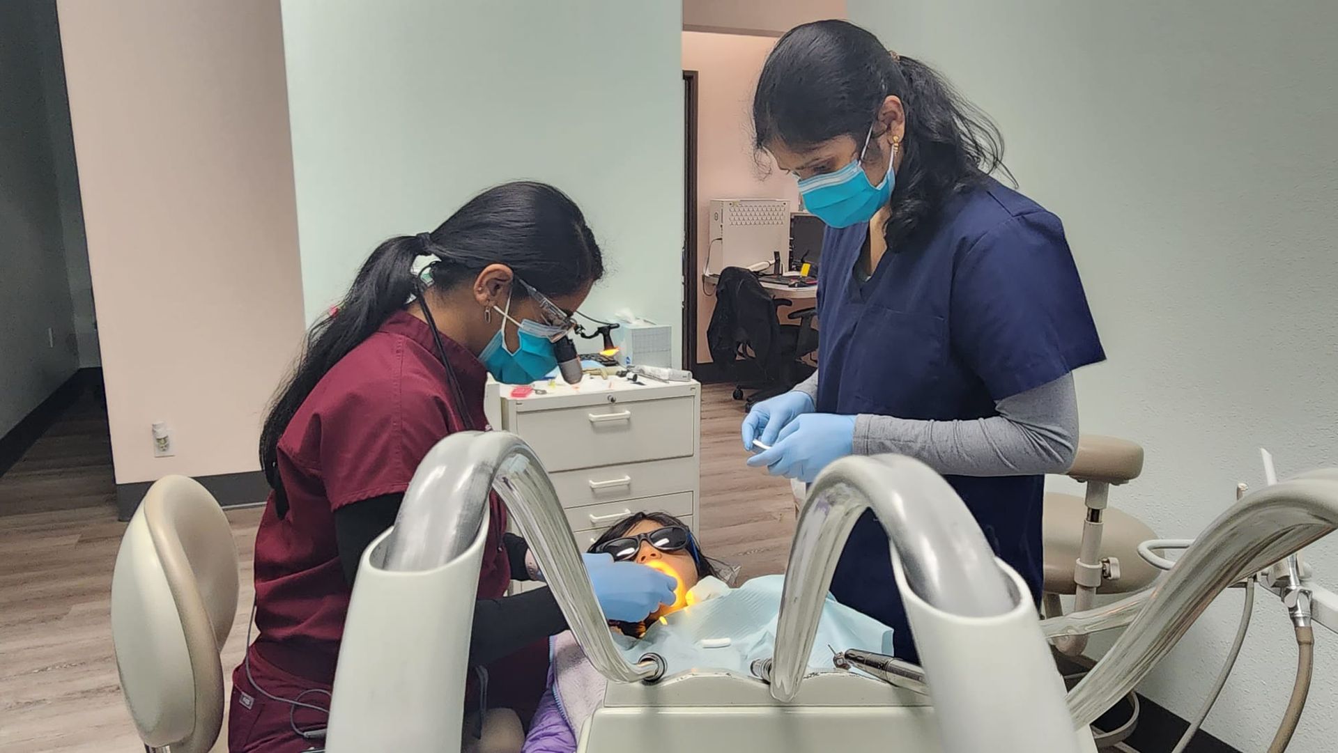 Two female dentists are working on a patient in a dental office.