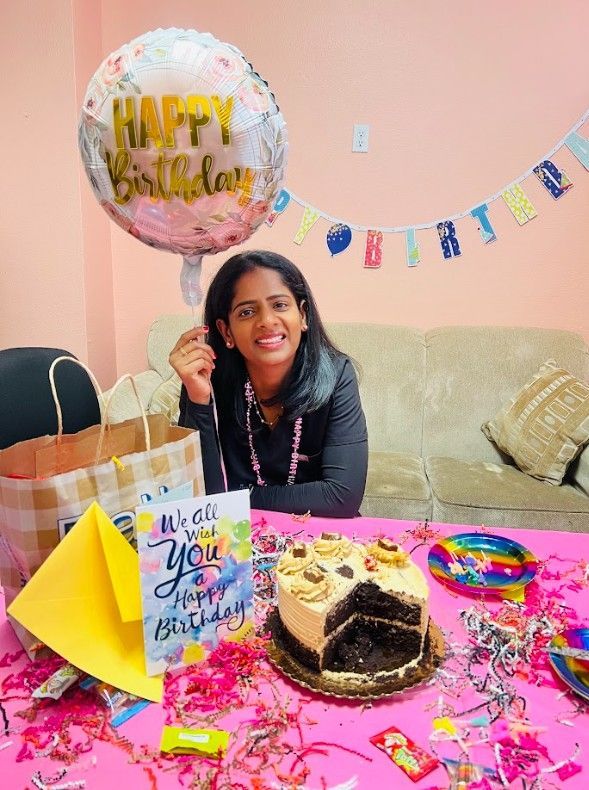 A woman is sitting at a table with a cake and a balloon.
