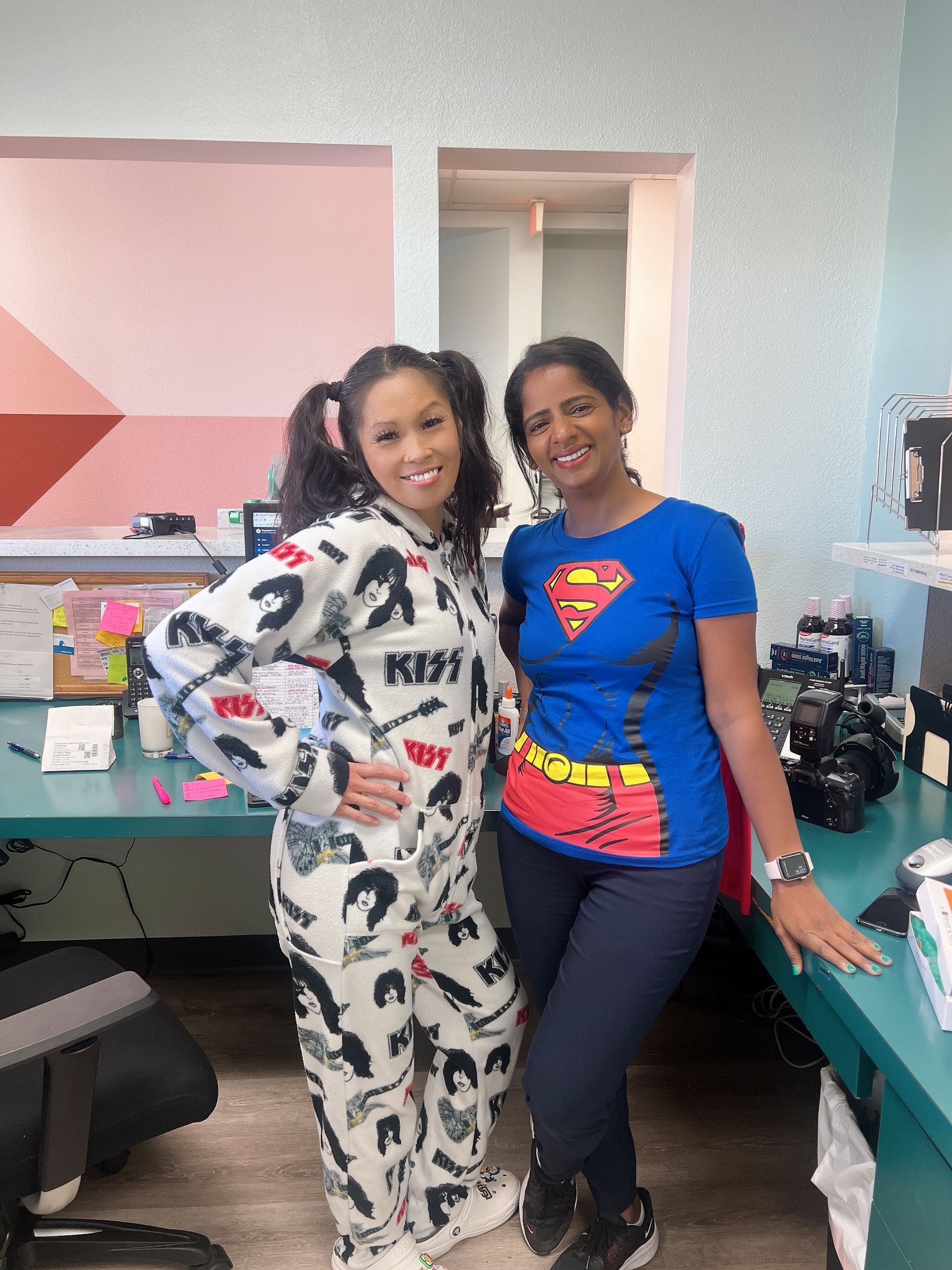 Two women are posing for a picture in an office . one of the women is wearing a superman shirt.