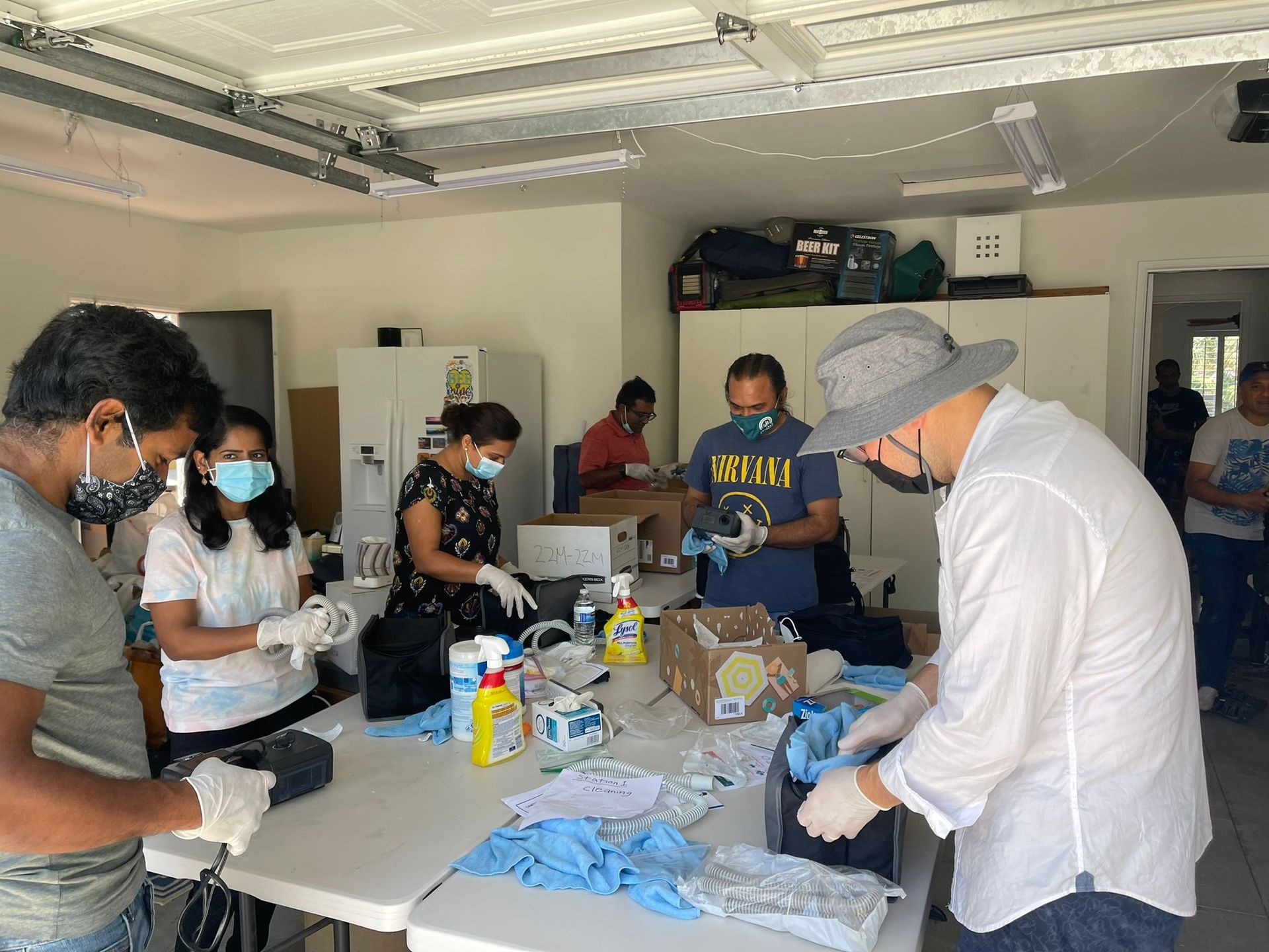 A group of people wearing masks and gloves are standing around a table in a garage.