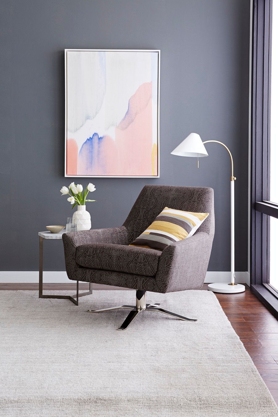 Cozy living room with patterned swivel chair, art, floor lamp, and a vase of flowers.
