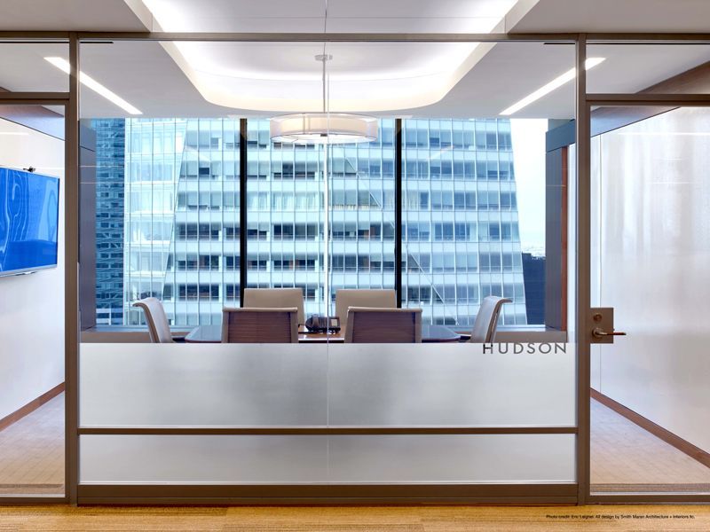 Glass-walled office with a desk, chairs, and a city view. The word